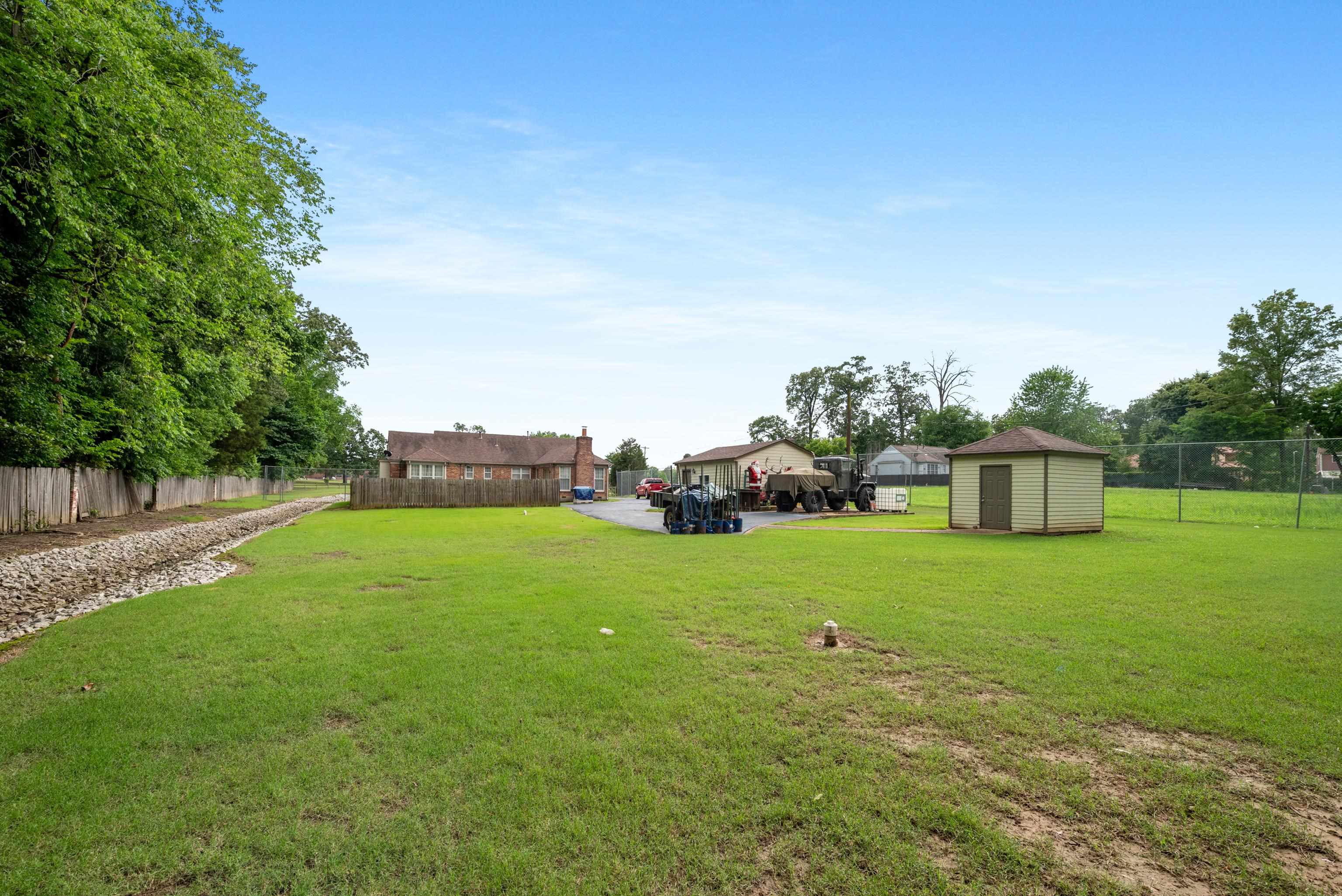 Grassy backyard with a small shed, fenced yard, and rock-lined drainage channel.