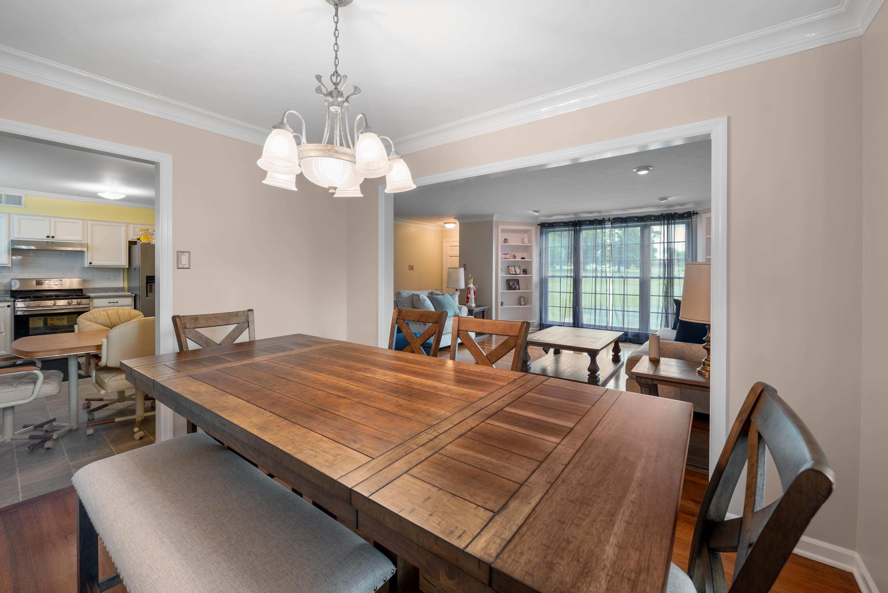 Dining room with a large rustic wooden table, chandelier, and open views into the kitchen and living room.