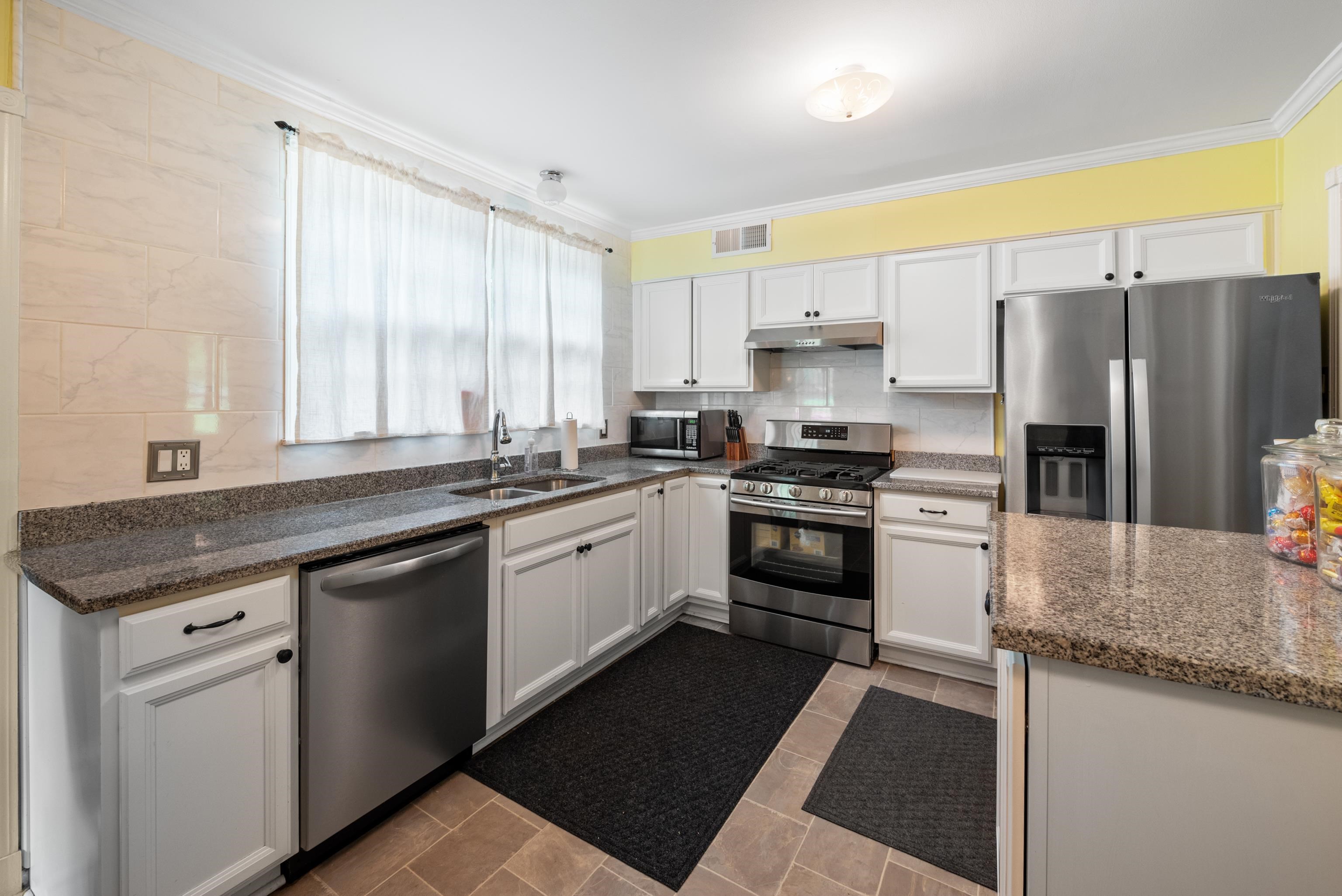 Kitchen with white cabinets, granite counters, stainless steel appliances, and a large curtained window.