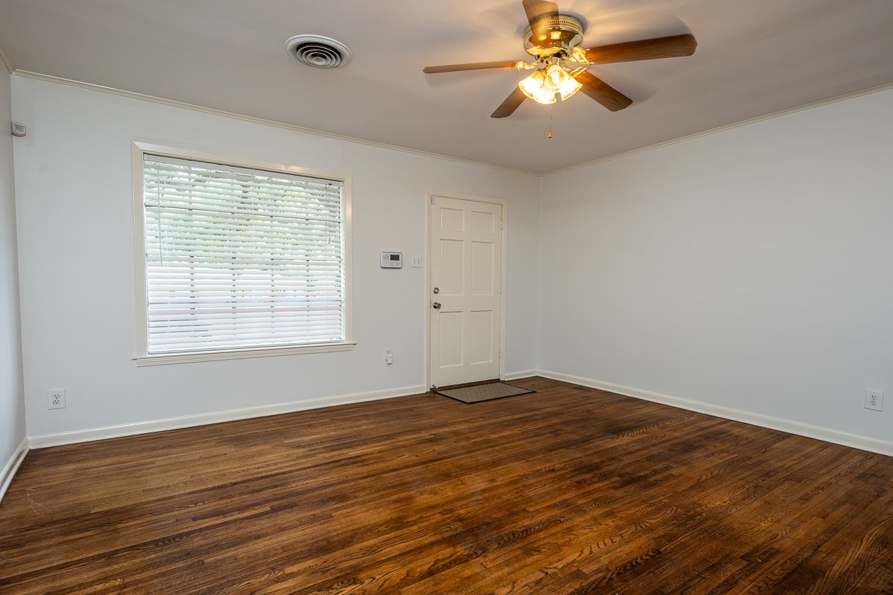 Empty room with dark hardwood floors, a window with white blinds, and a ceiling fan.