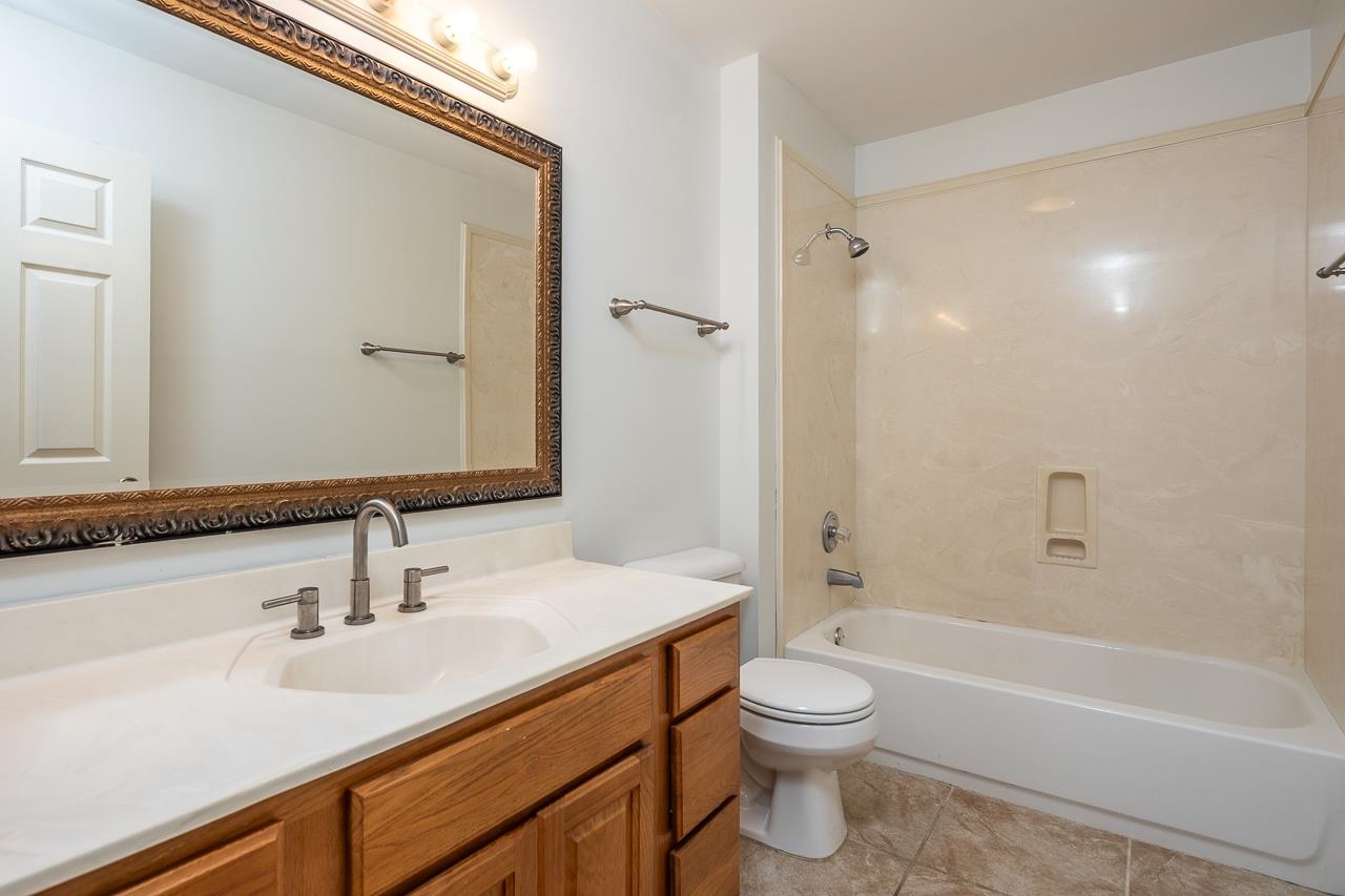 Bathroom with a wood vanity, ornate mirror, and beige-tiled tub and shower.