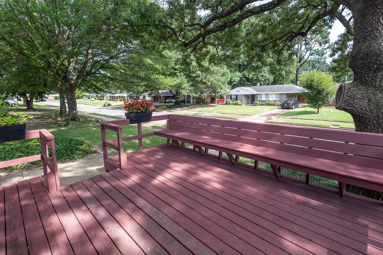 Shaded wooden deck with built-in benches and flower planters overlooking a residential street.