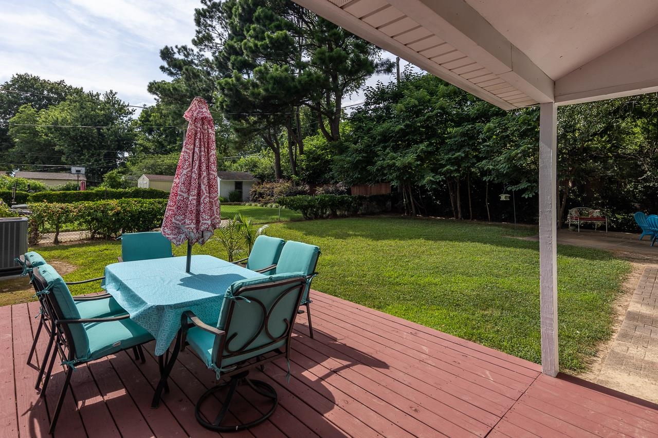Backyard patio with a covered red deck, turquoise dining set, and tree-lined lawn.
