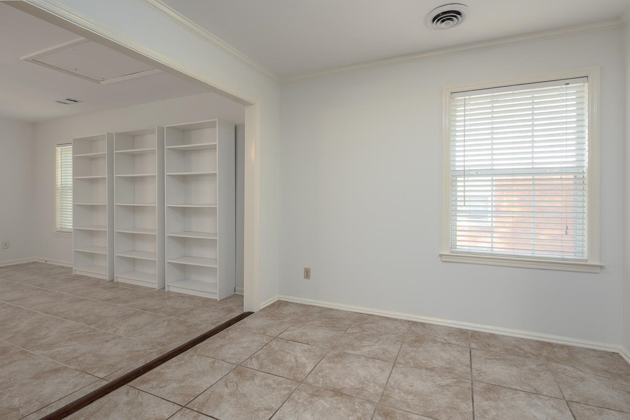 Empty tiled room with a large window and white shelving units in the adjoining area.