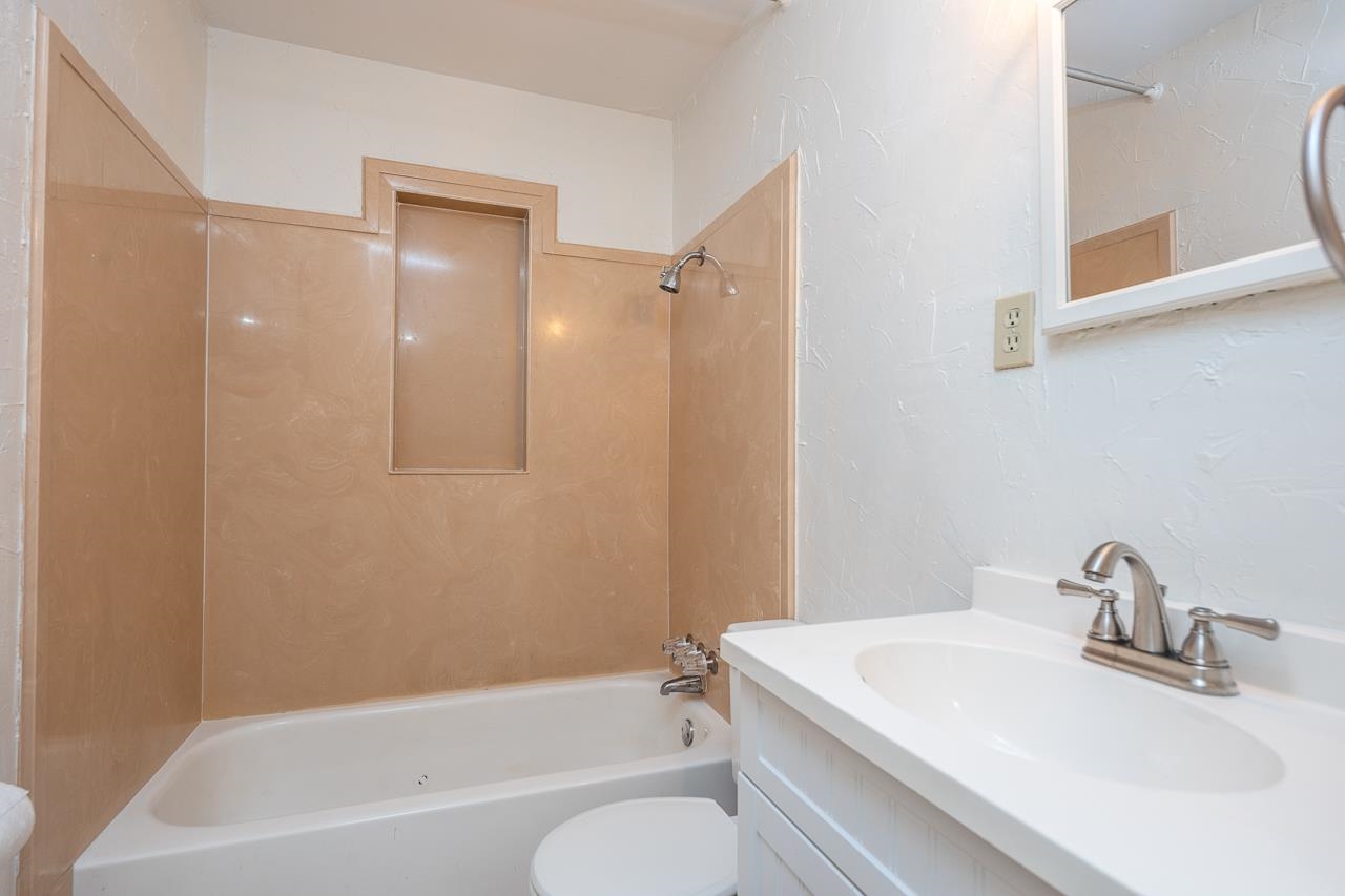 Bathroom with a tan tub surround, built-in niche, and white vanity.