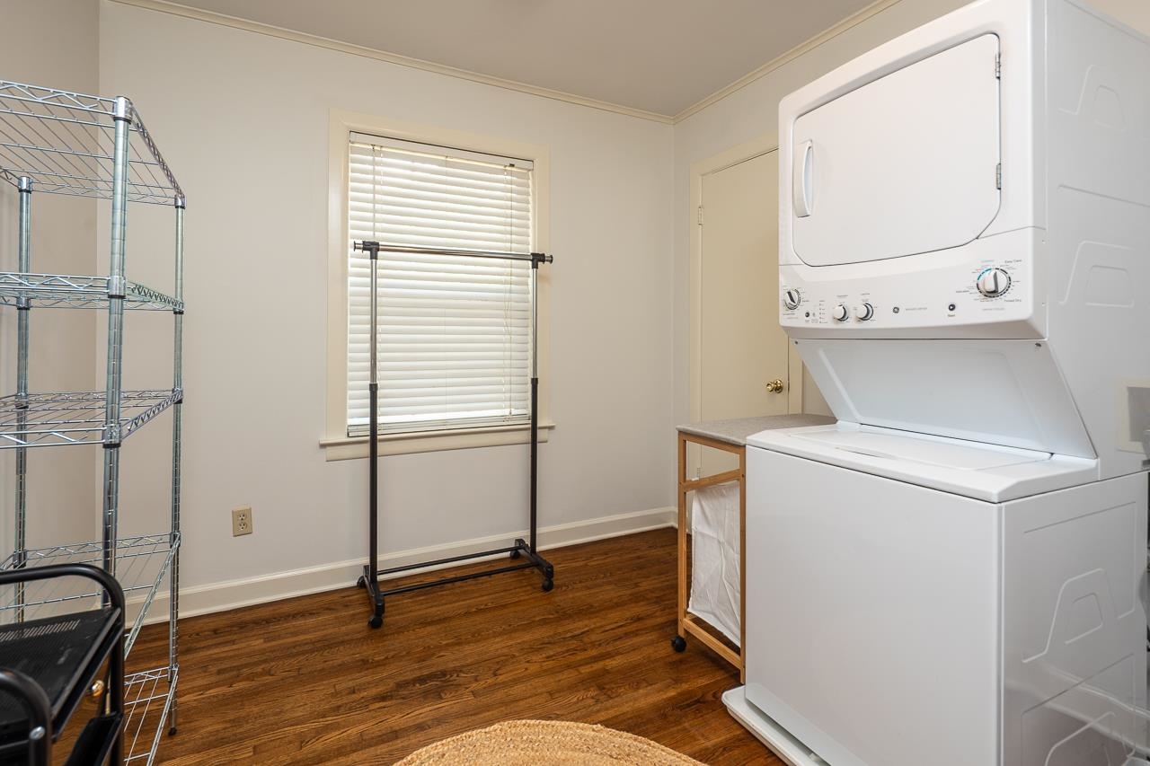 Laundry room with stacked washer and dryer, wire shelving, and wood floors.