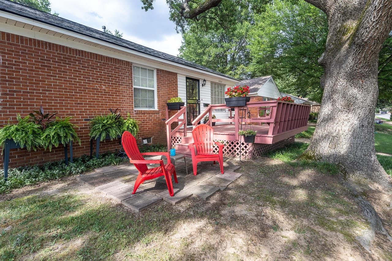 Brick home with a raised pink deck, red patio chairs, and a large shade tree.