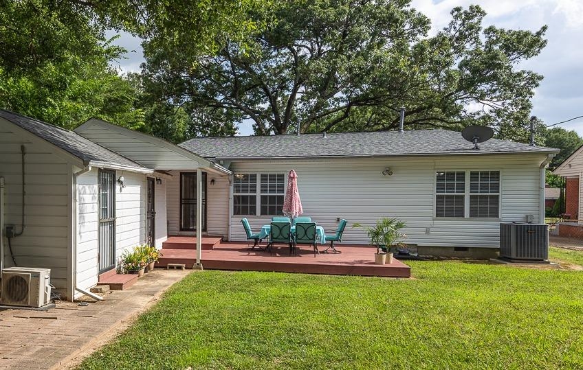 Rear of a light-sided house with a red deck, turquoise patio chairs, and a leafy lawn.