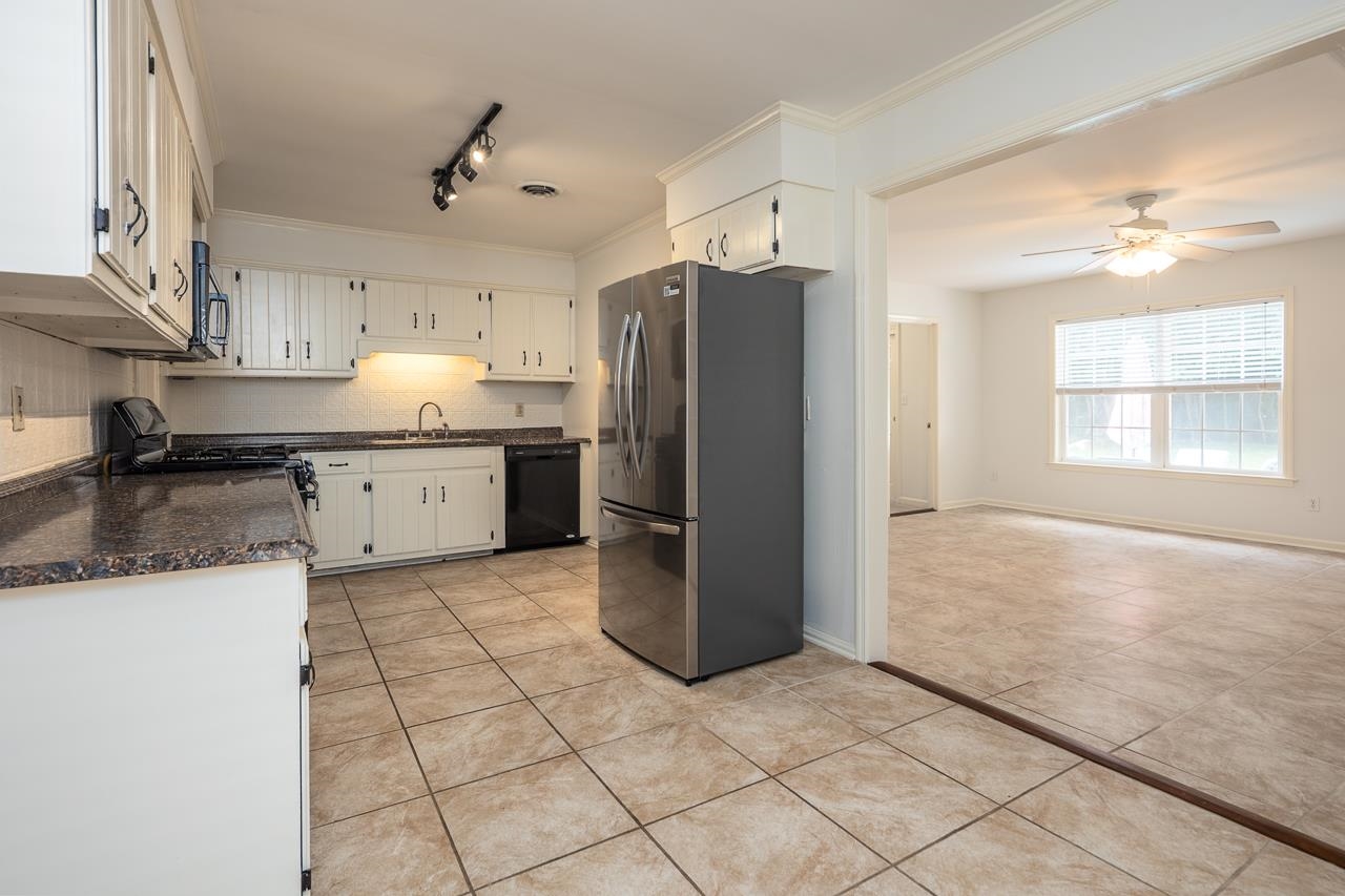 Kitchen with white cabinets, granite counters, stainless steel refrigerator, and an open adjoining room.