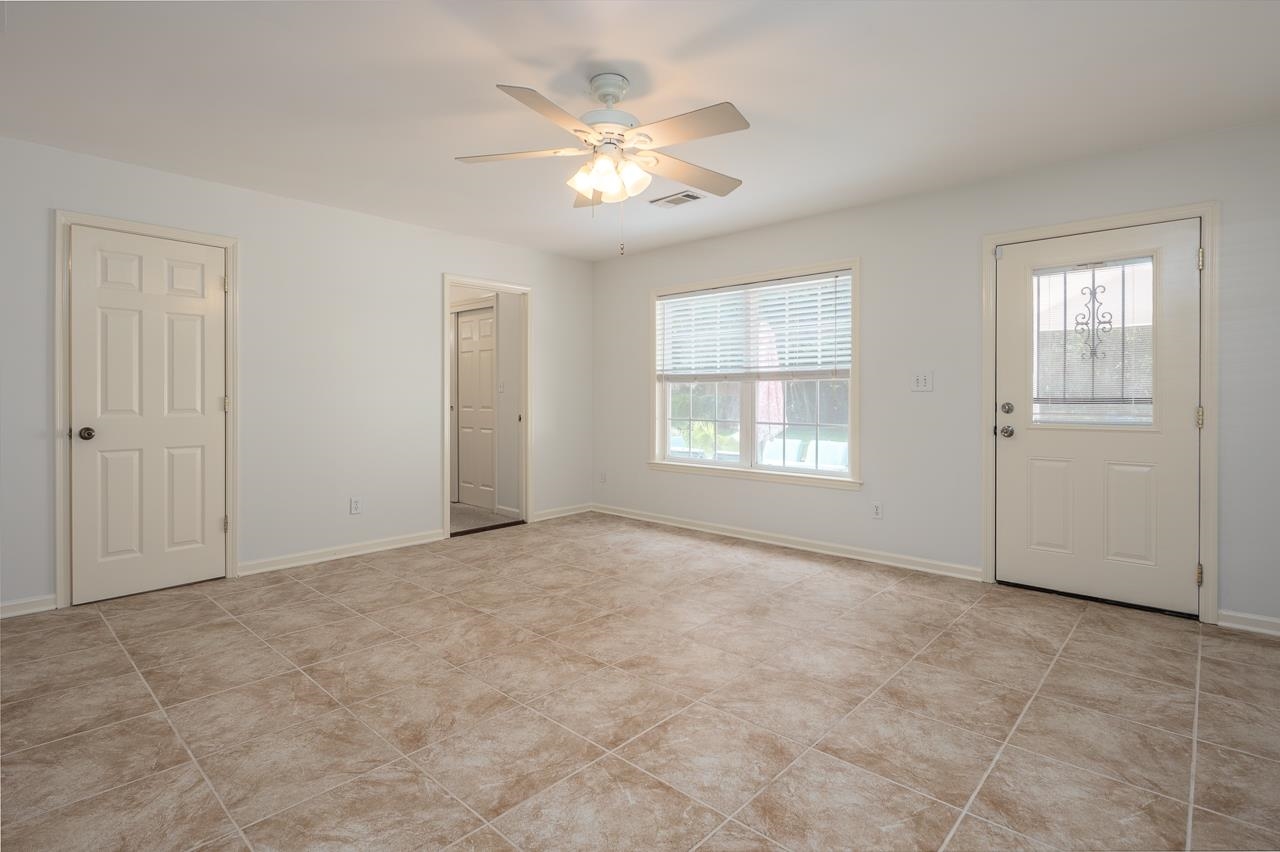 Empty tiled room with a ceiling fan, window with blinds, and exterior door.