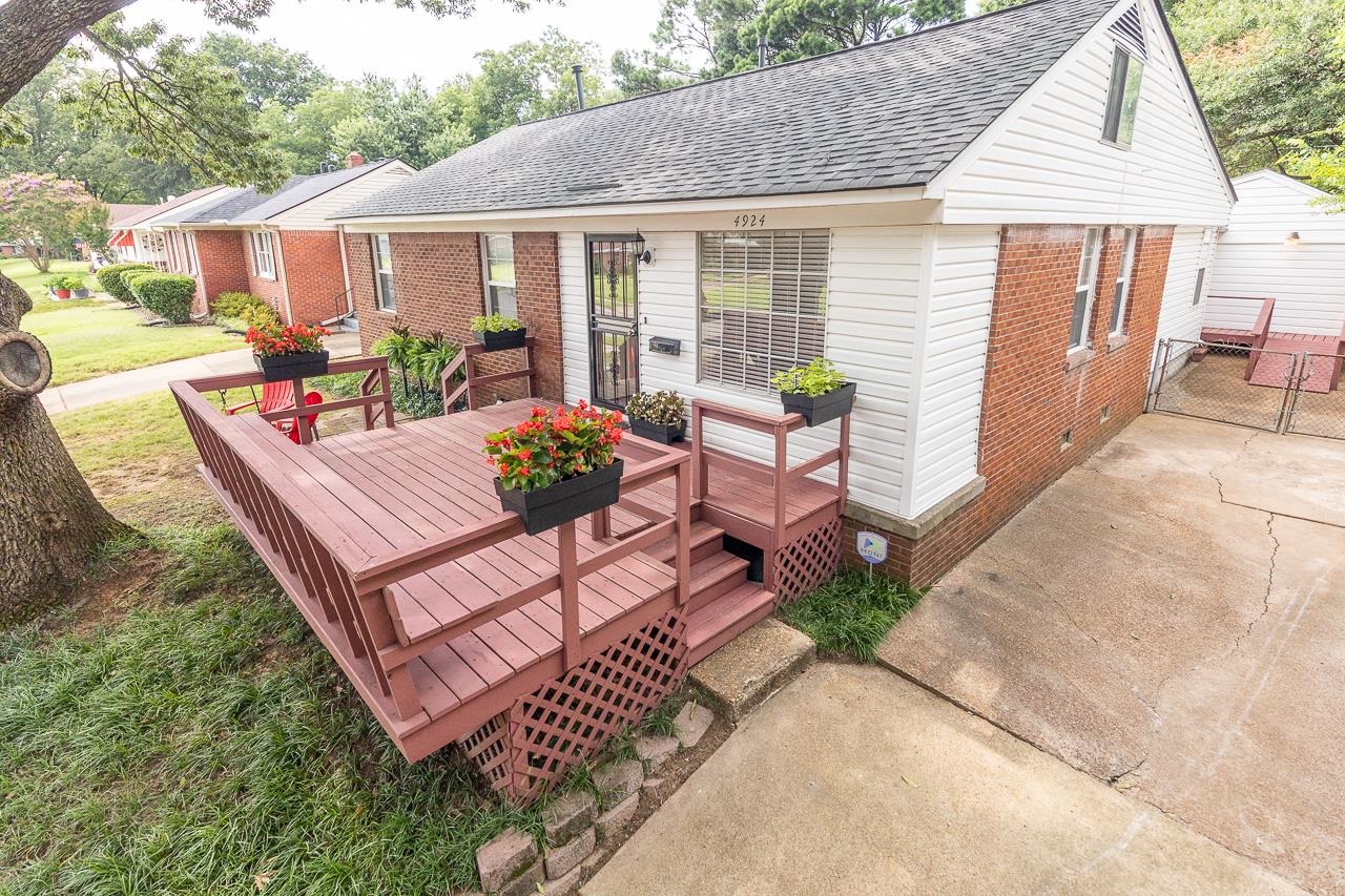 Brick-and-siding house with a raised wooden deck, flower planters, and a concrete driveway.
