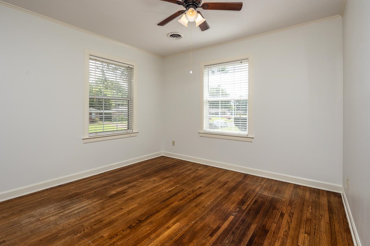 Empty room with polished hardwood floors, two windows with blinds, and a ceiling fan.