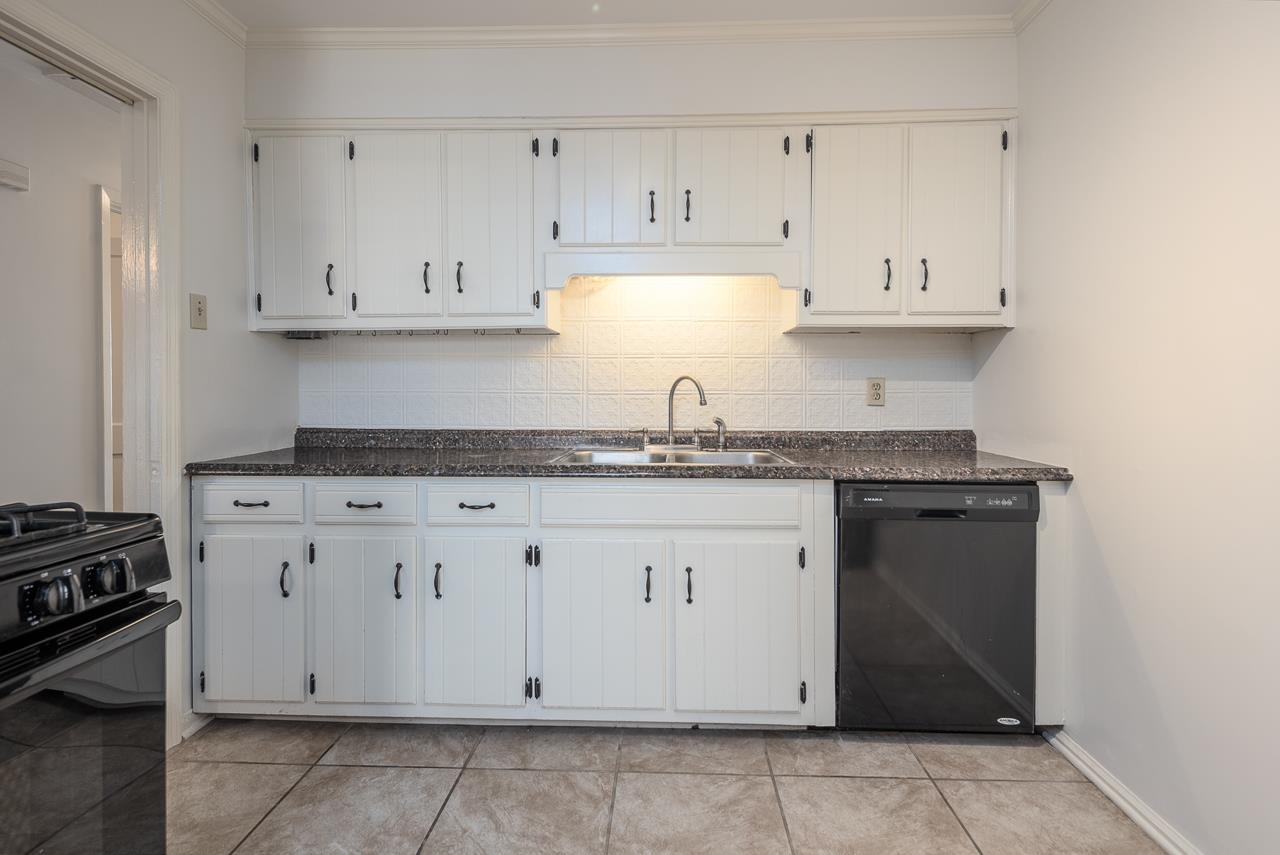 Kitchen with white paneled cabinets, dark granite counters, a double-basin sink, and a black dishwasher.