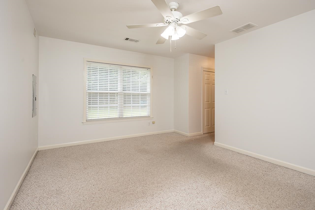 Empty bedroom with beige carpet, a wide window with blinds, and a ceiling fan.
