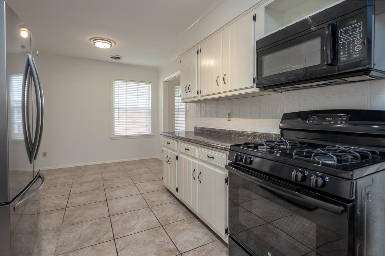 Kitchen with white cabinets, dark countertops, black gas range, and large square tile flooring.