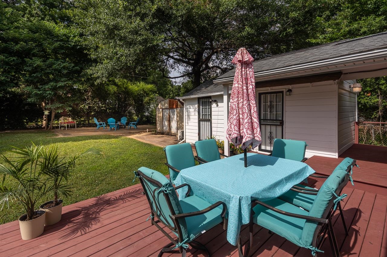 Back deck with turquoise dining set and umbrella beside a leafy yard.