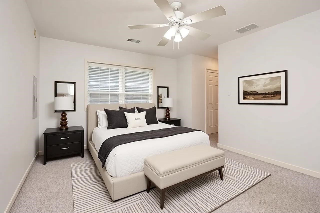 Staged bedroom with a white bed, charcoal accents, striped rug, and ceiling fan.