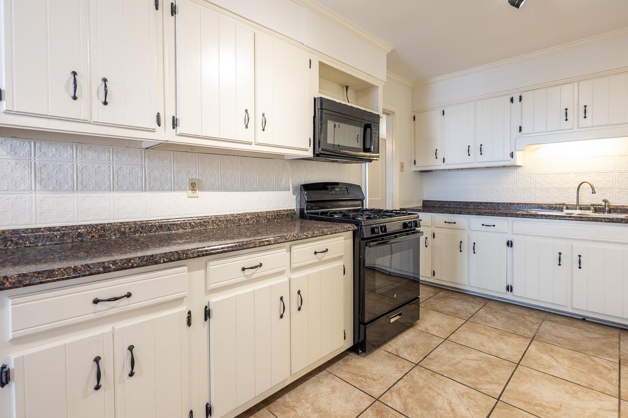 Kitchen with white cabinets, dark countertops, and a black range and microwave.