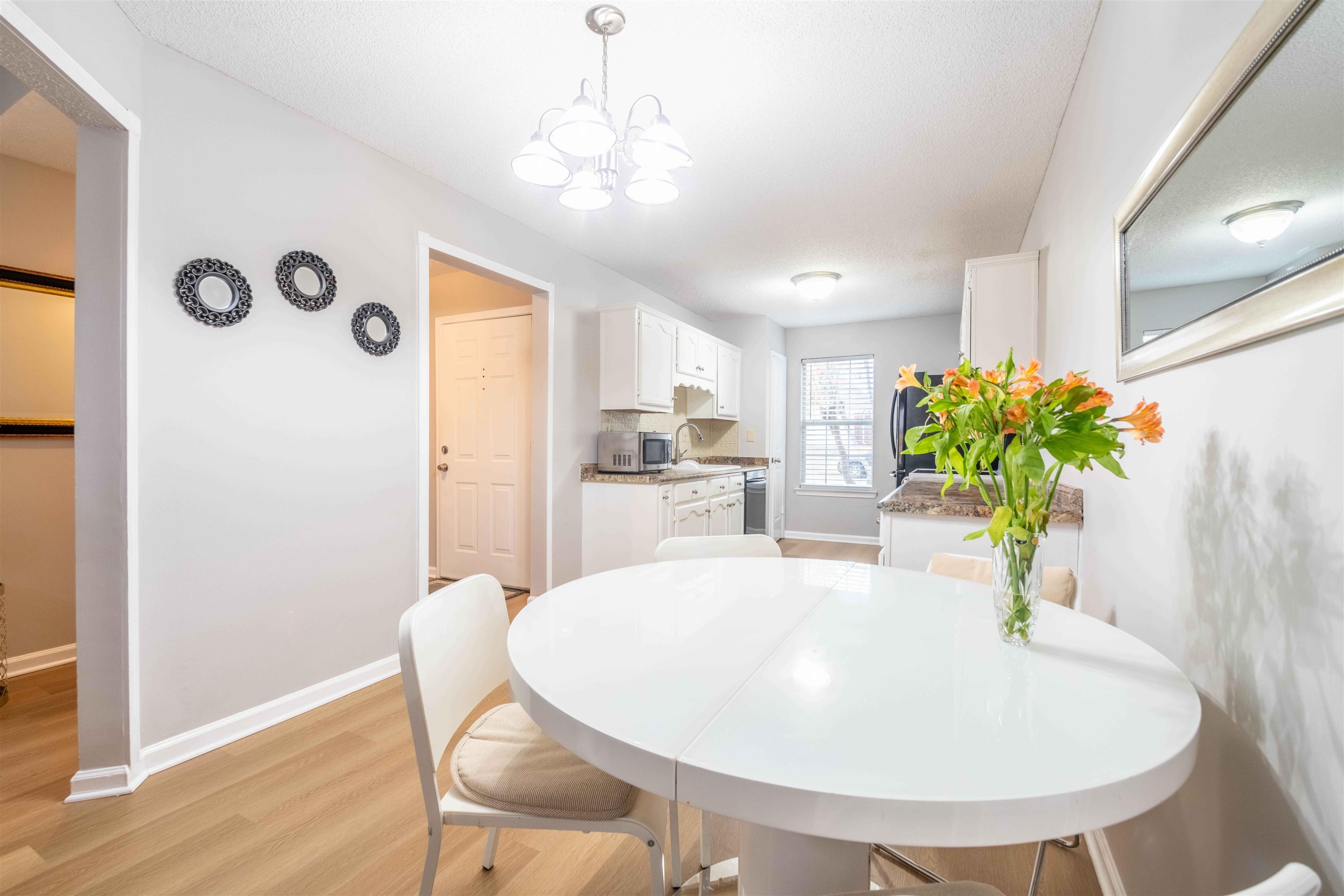 Dining area with a white oval table and orange flowers beside a compact kitchen.