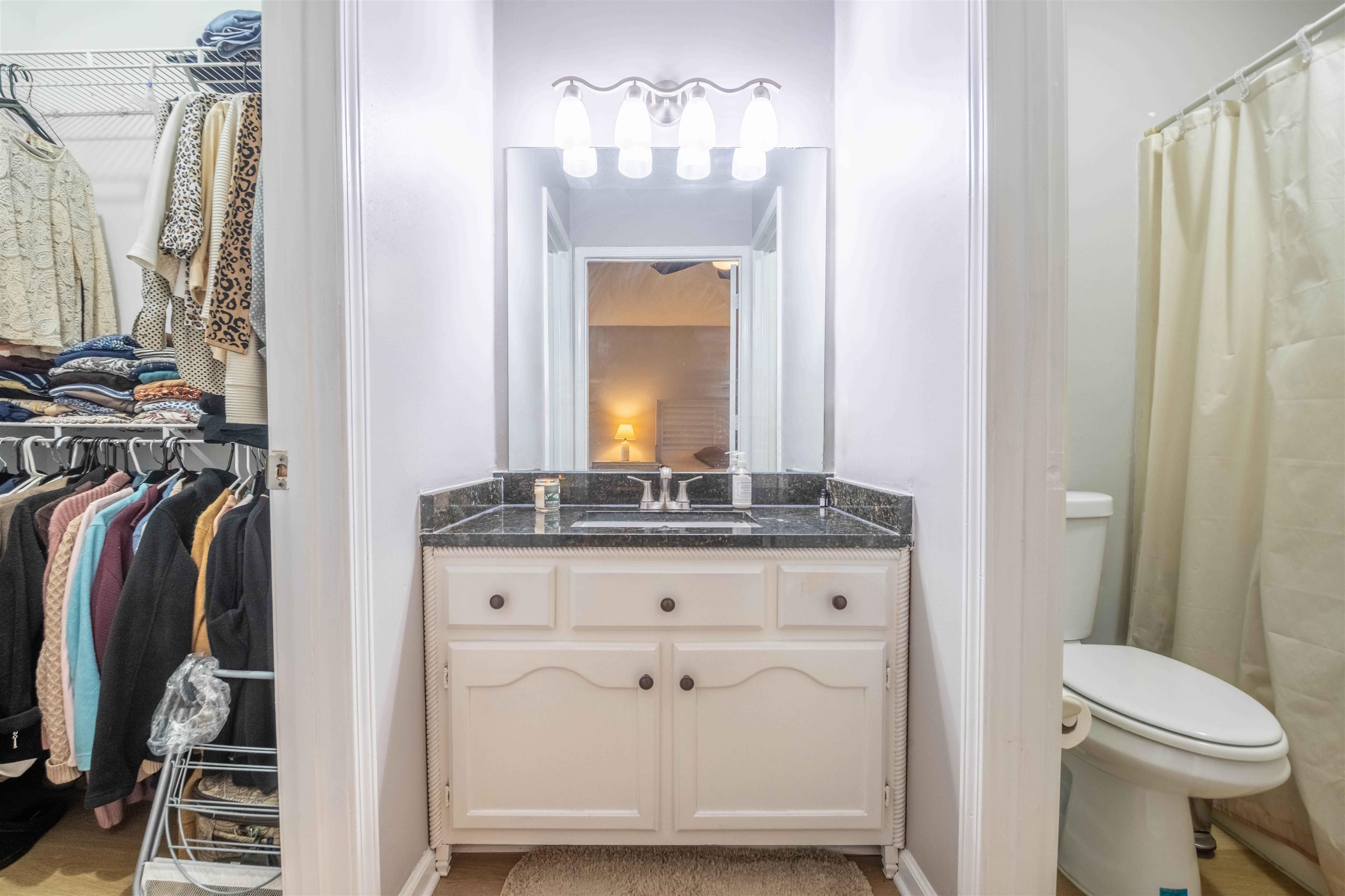 Bathroom vanity with dark stone countertop, beside an open closet and curtained shower.