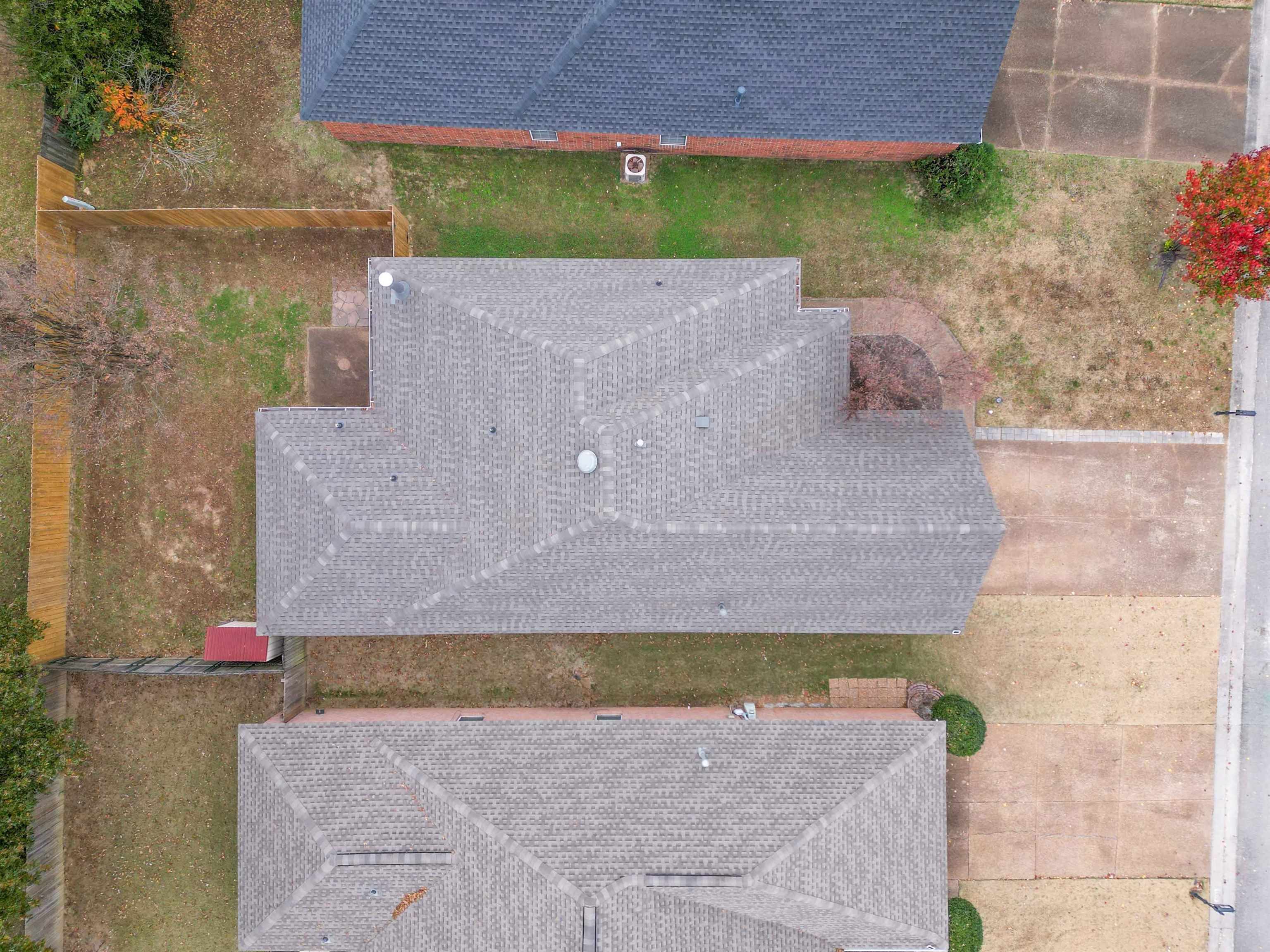Aerial view of a gray-shingled home, yard, driveway, and neighboring houses.