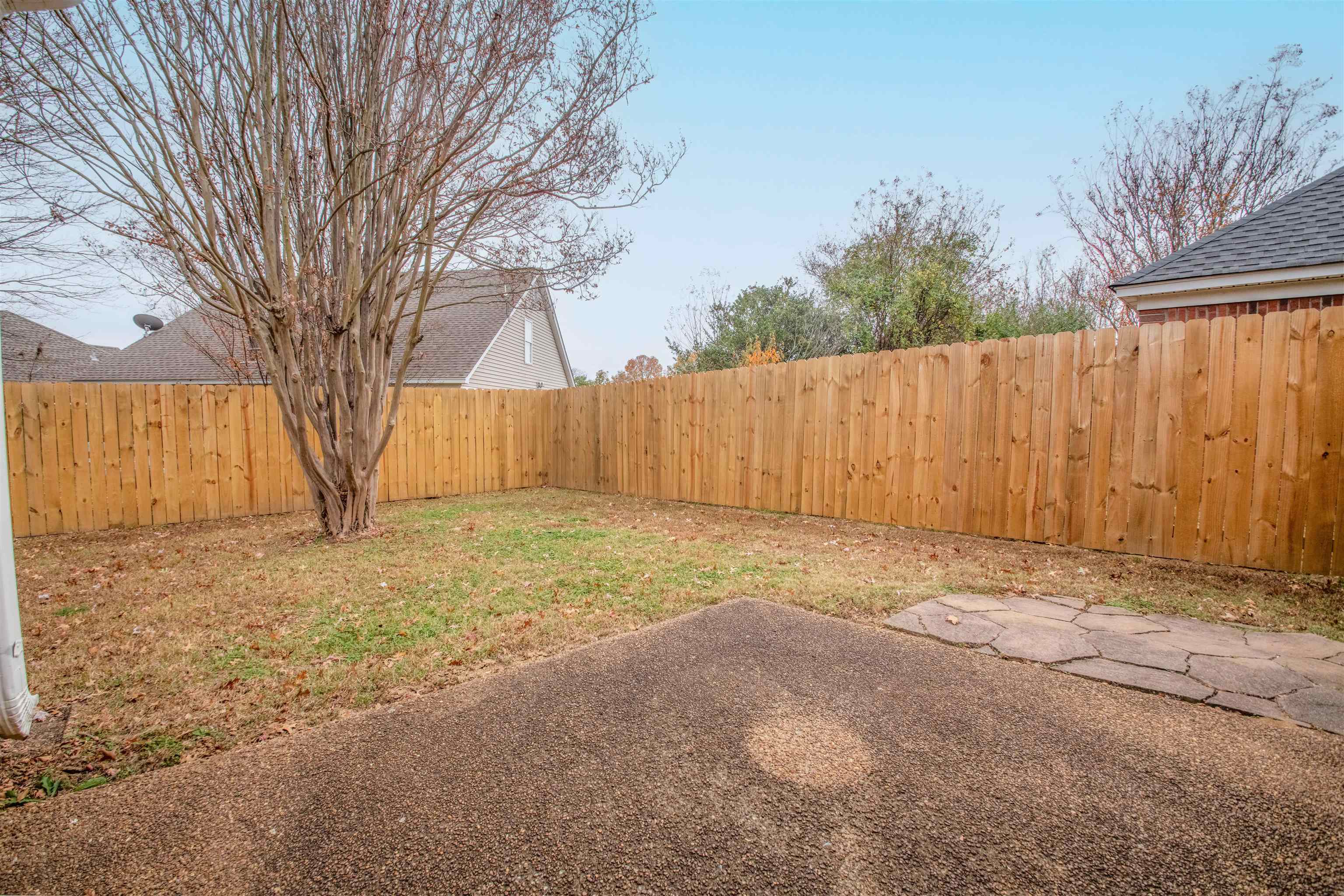 Fenced backyard with a large tree, patchy lawn, and paved patio.