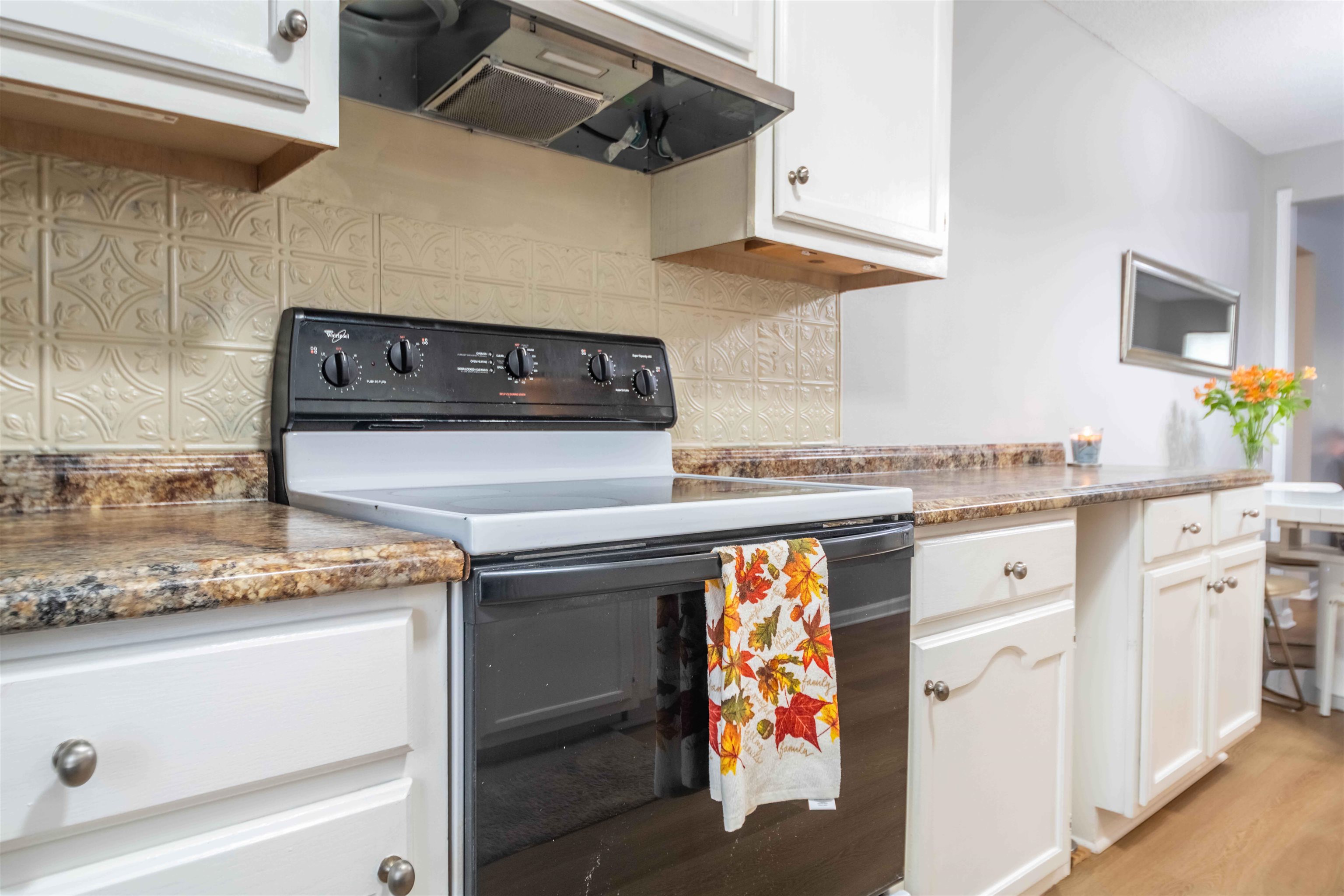 Kitchen range and oven beneath white cabinets, with patterned tile backsplash and autumn-leaf towel.