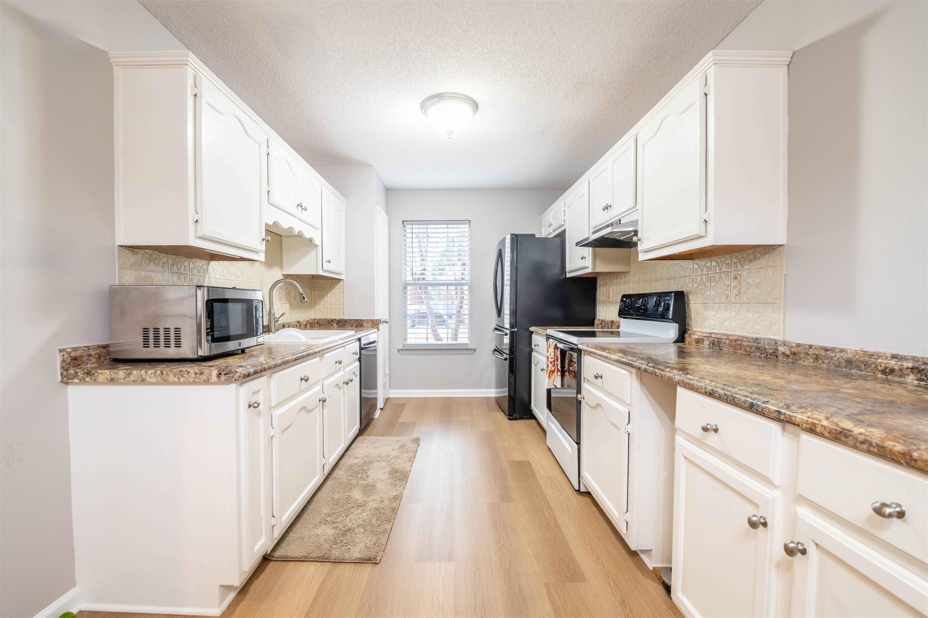 Galley kitchen with white cabinets, patterned tile backsplash, and dark appliances.