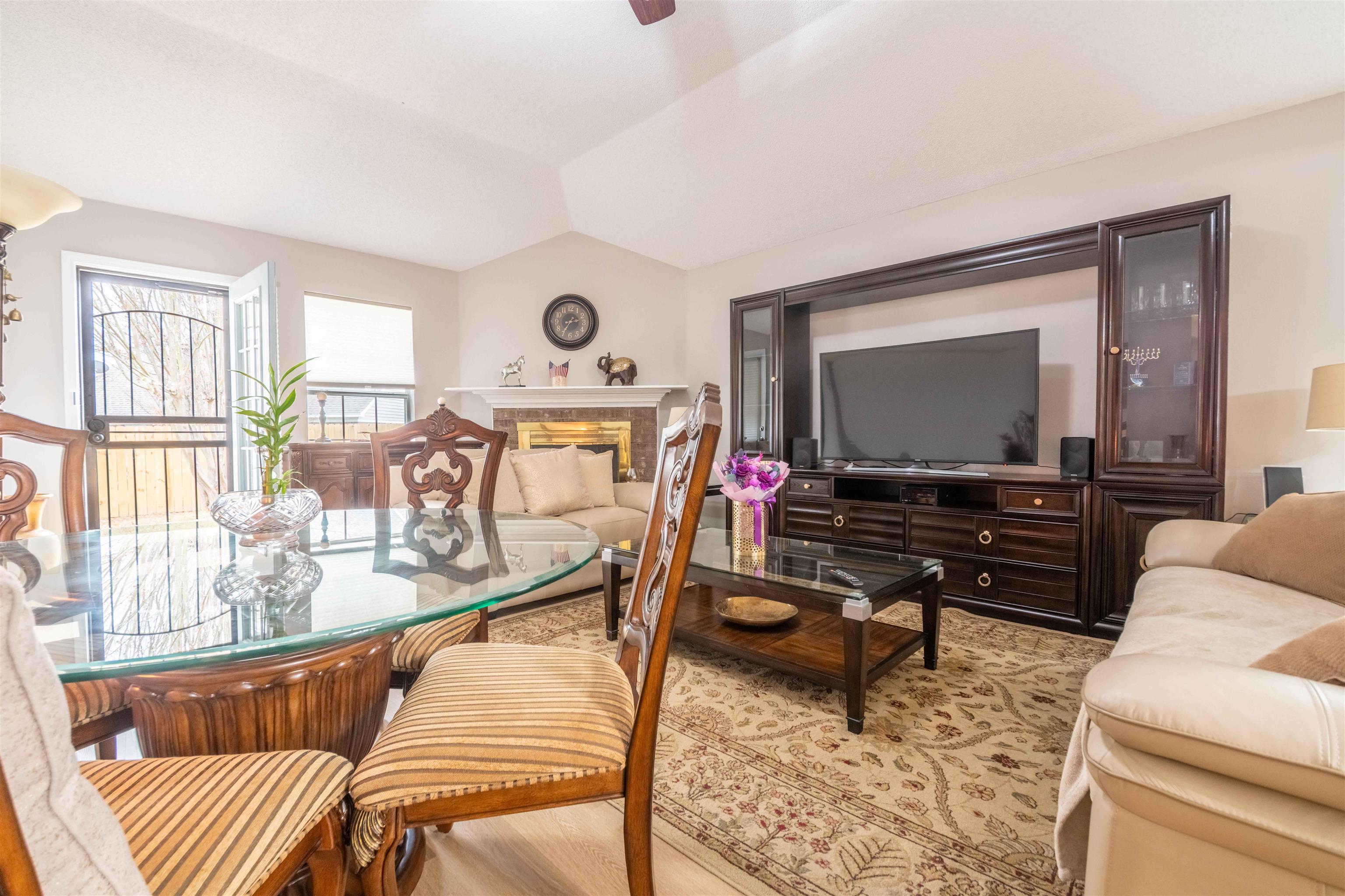 Furnished living and dining area with a fireplace, glass-top table, and large television.