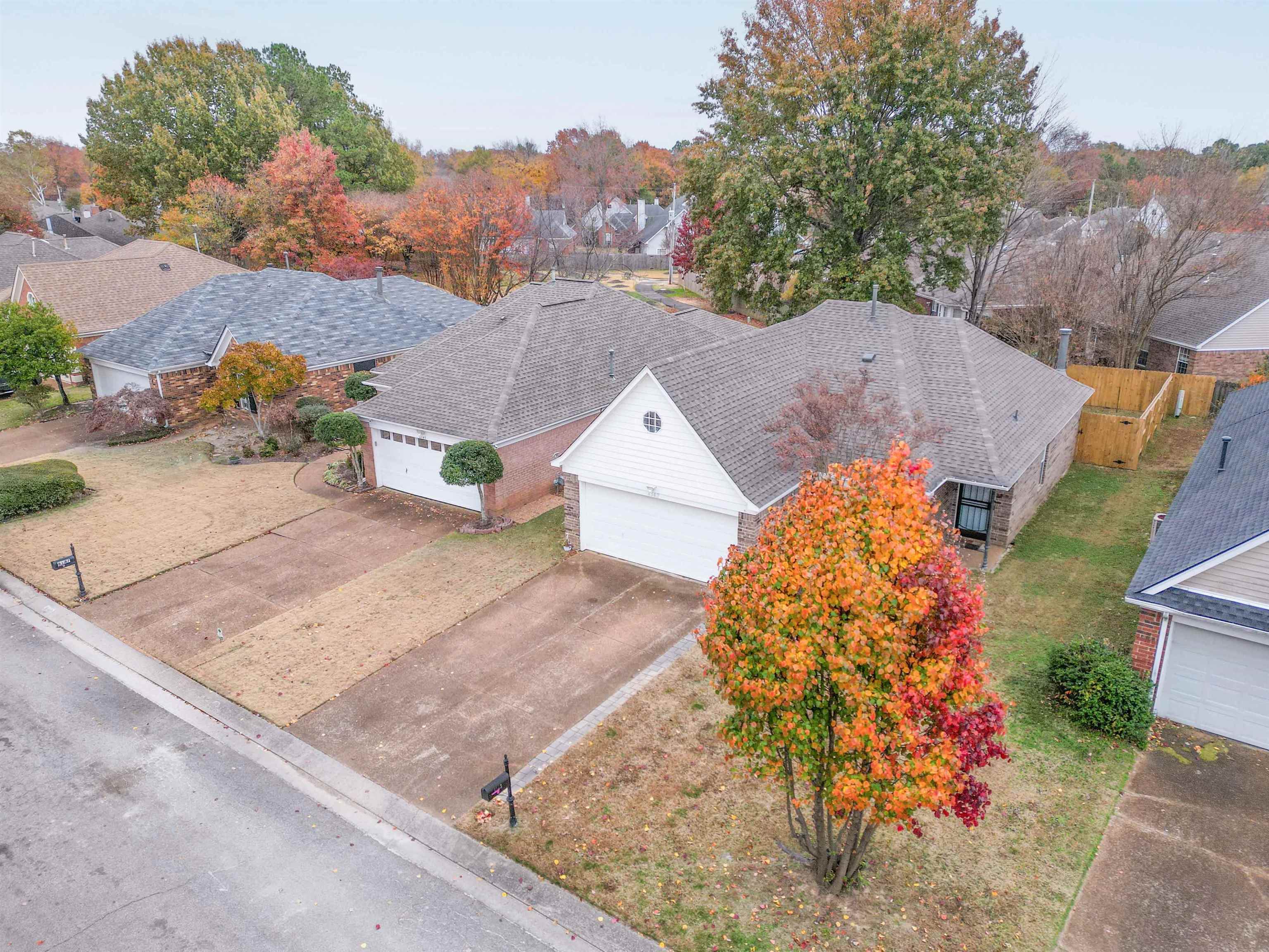 Aerial view of a brick house with two garages and a brightly colored autumn tree in front.