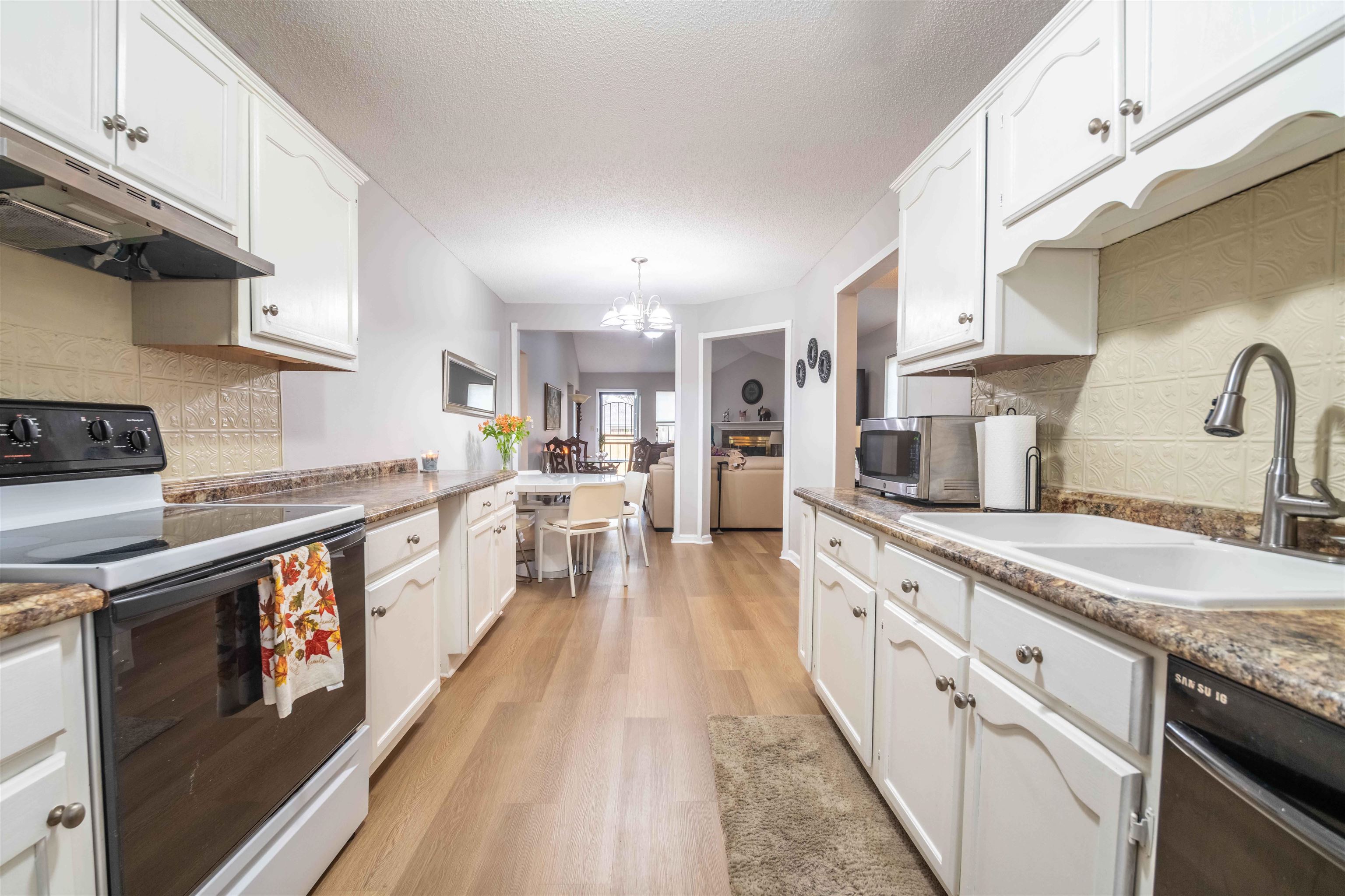 Galley kitchen with white cabinets, patterned backsplash, and counters opening toward the dining and living areas.