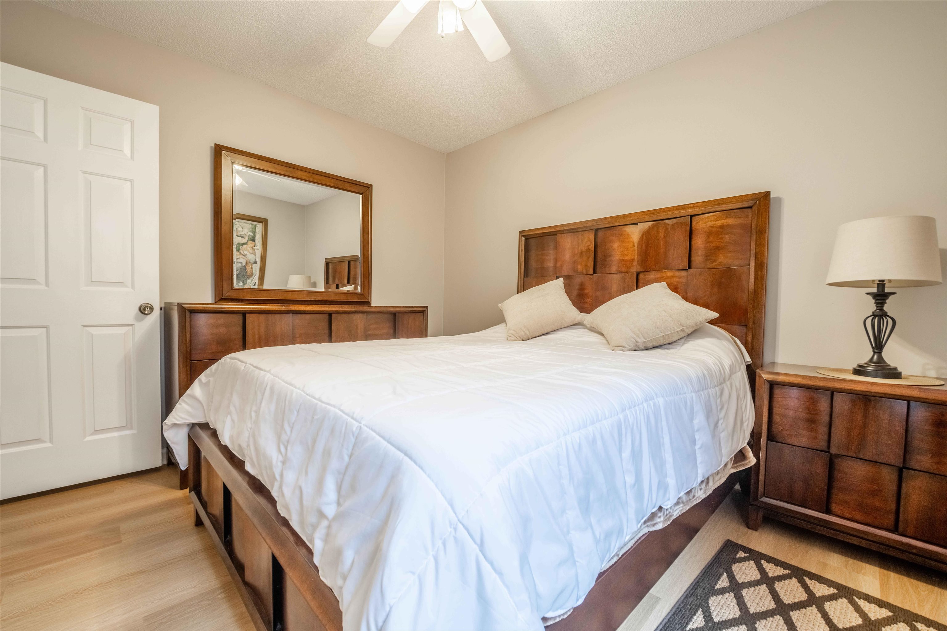 Bedroom with white bedding, dark wood furniture, a large mirror, and a bedside lamp.