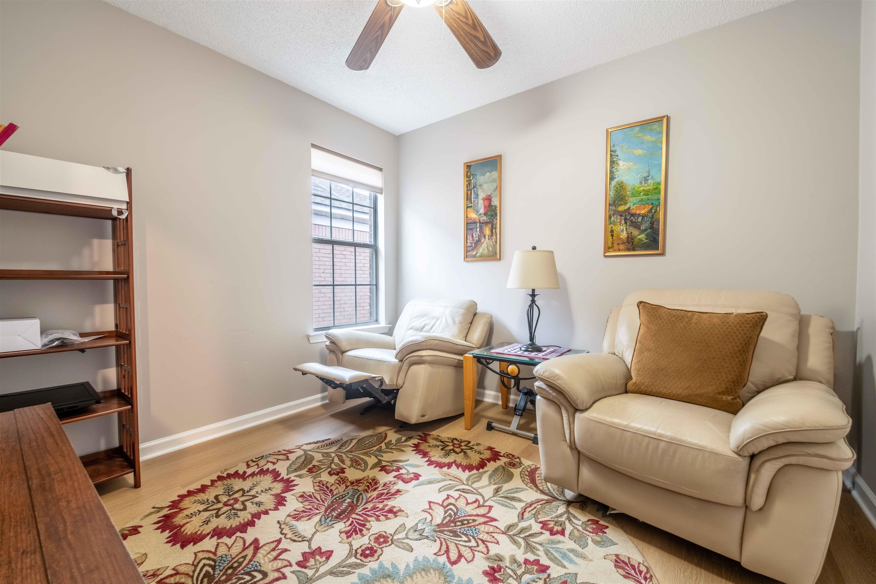 Living room with cream leather seating, a floral rug, and a vaulted ceiling with a ceiling fan.