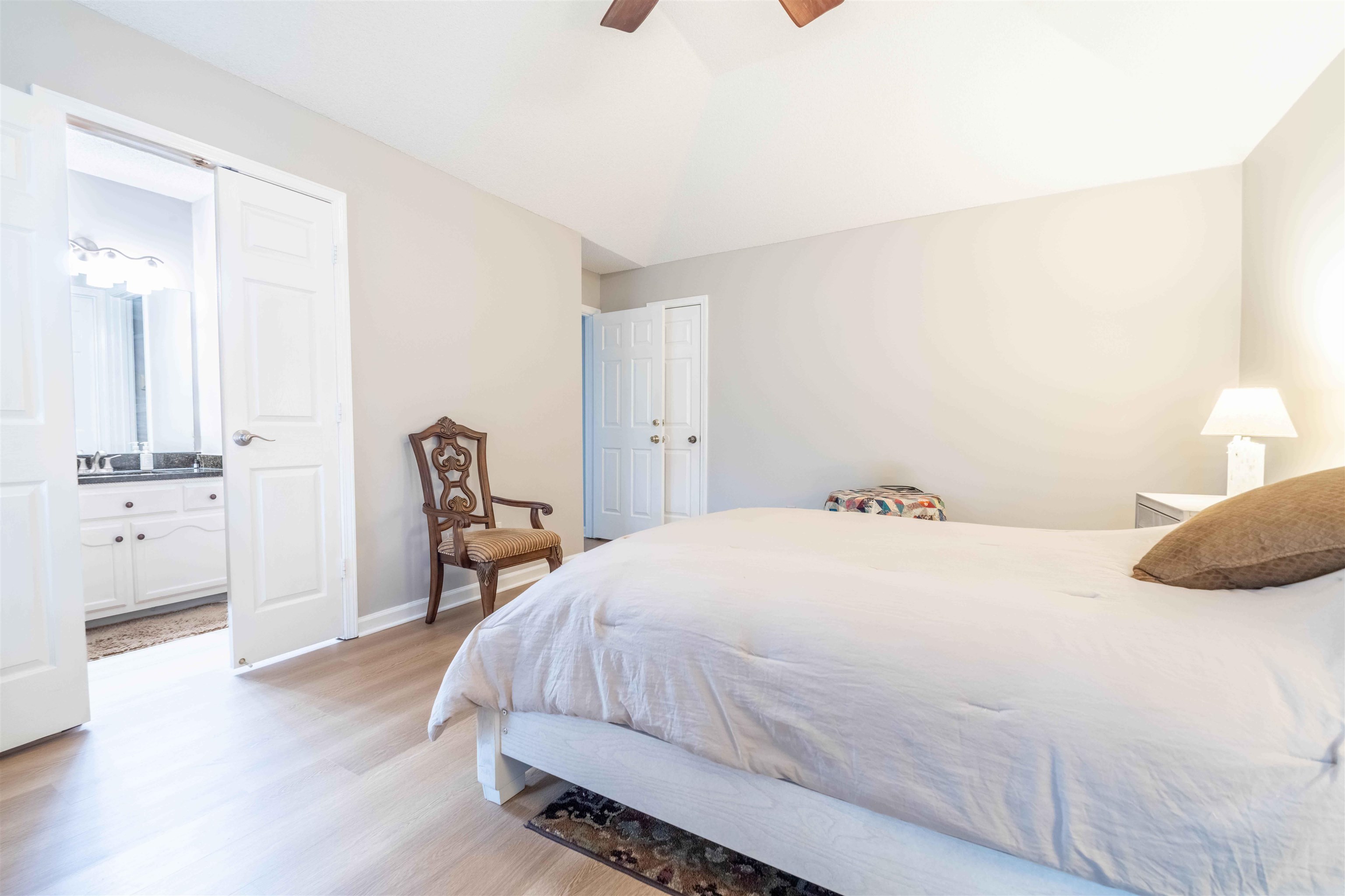 Furnished bedroom with a large white bed and an adjoining bathroom visible through the open doorway.