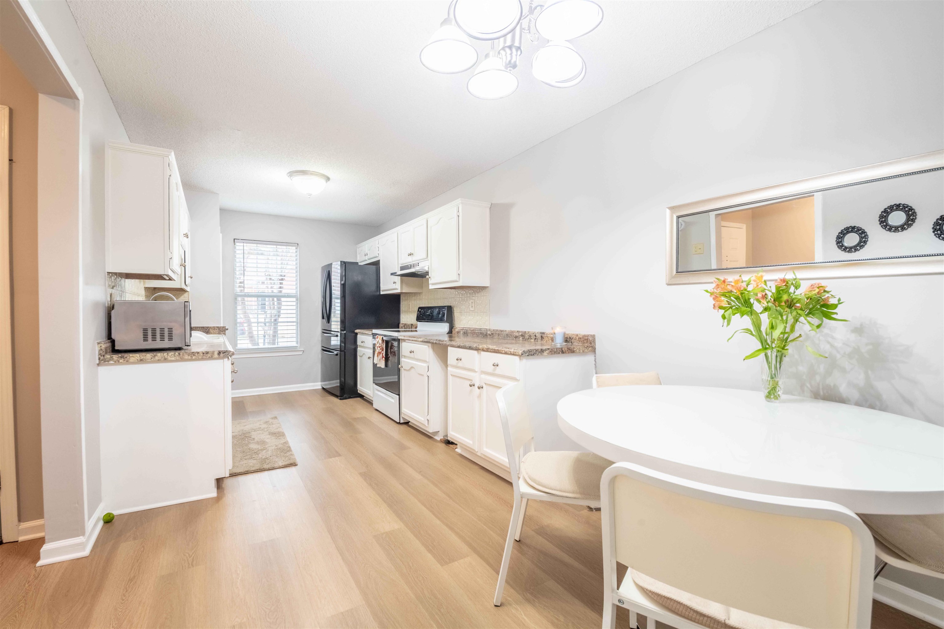 Bright kitchen and dining area with white cabinets, black appliances, and a round table beneath a wall mirror.