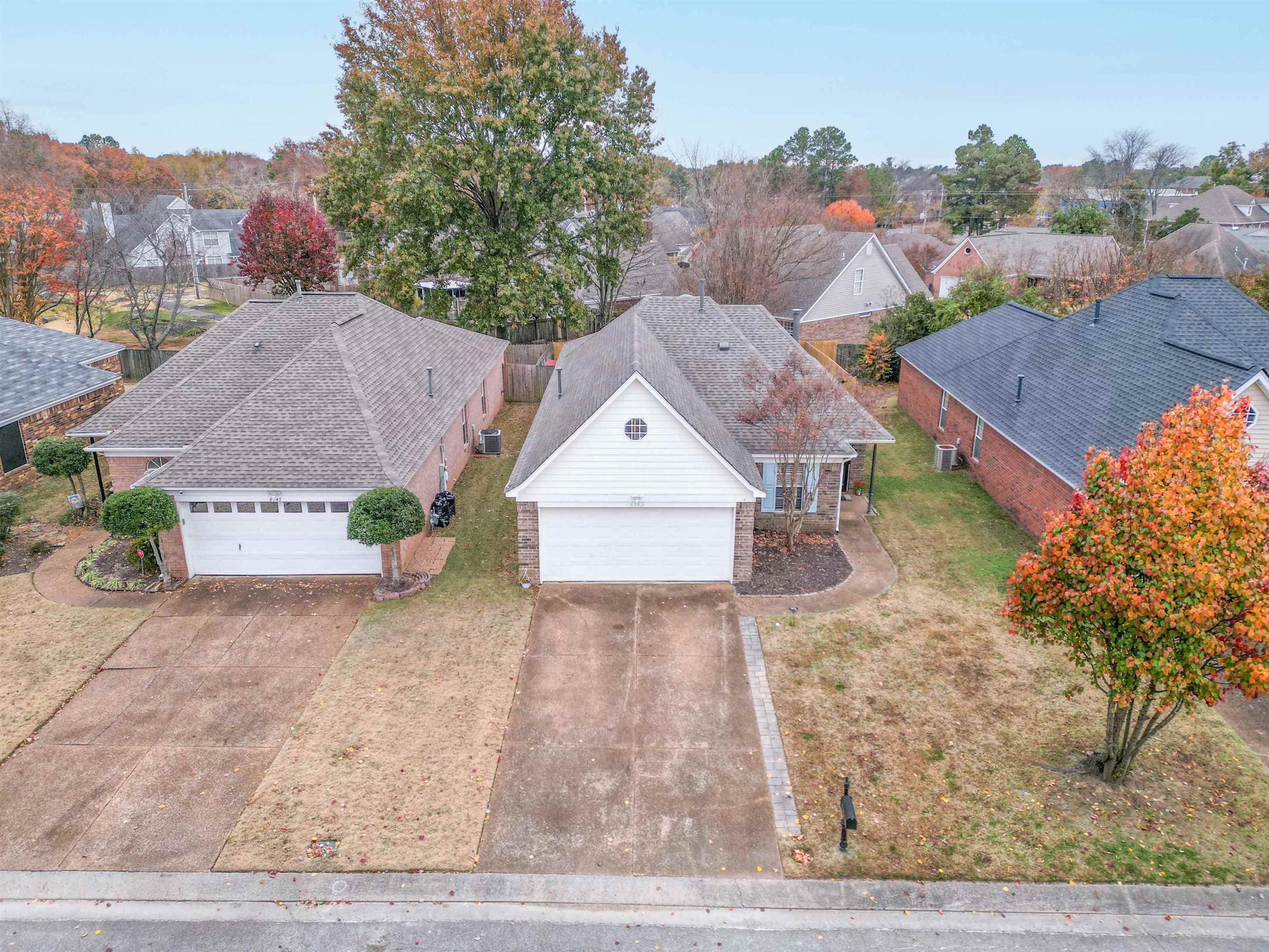 Aerial view of a brick house with a white garage door and driveway among autumn trees.