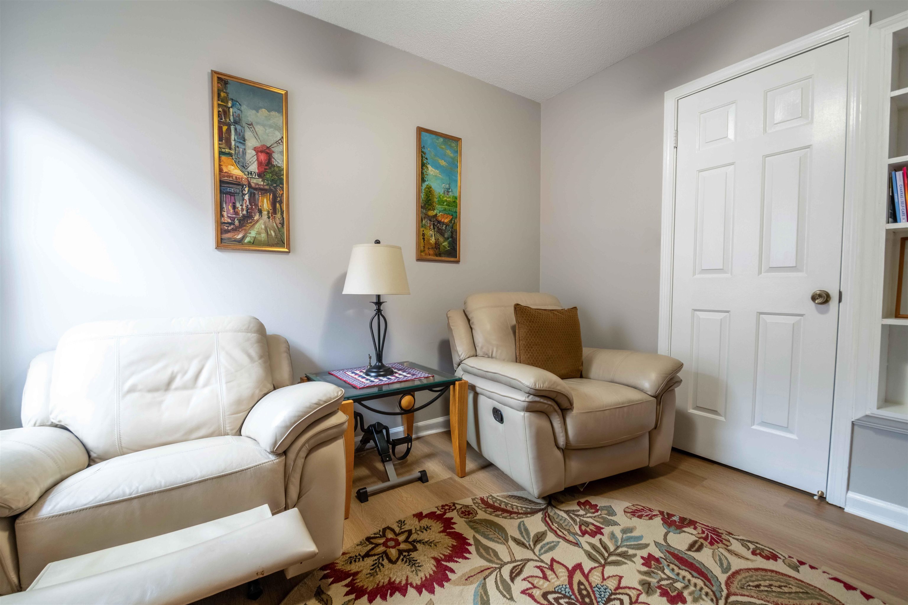 Living room with two leather recliners, a glass-top table, framed art, and a floral rug.