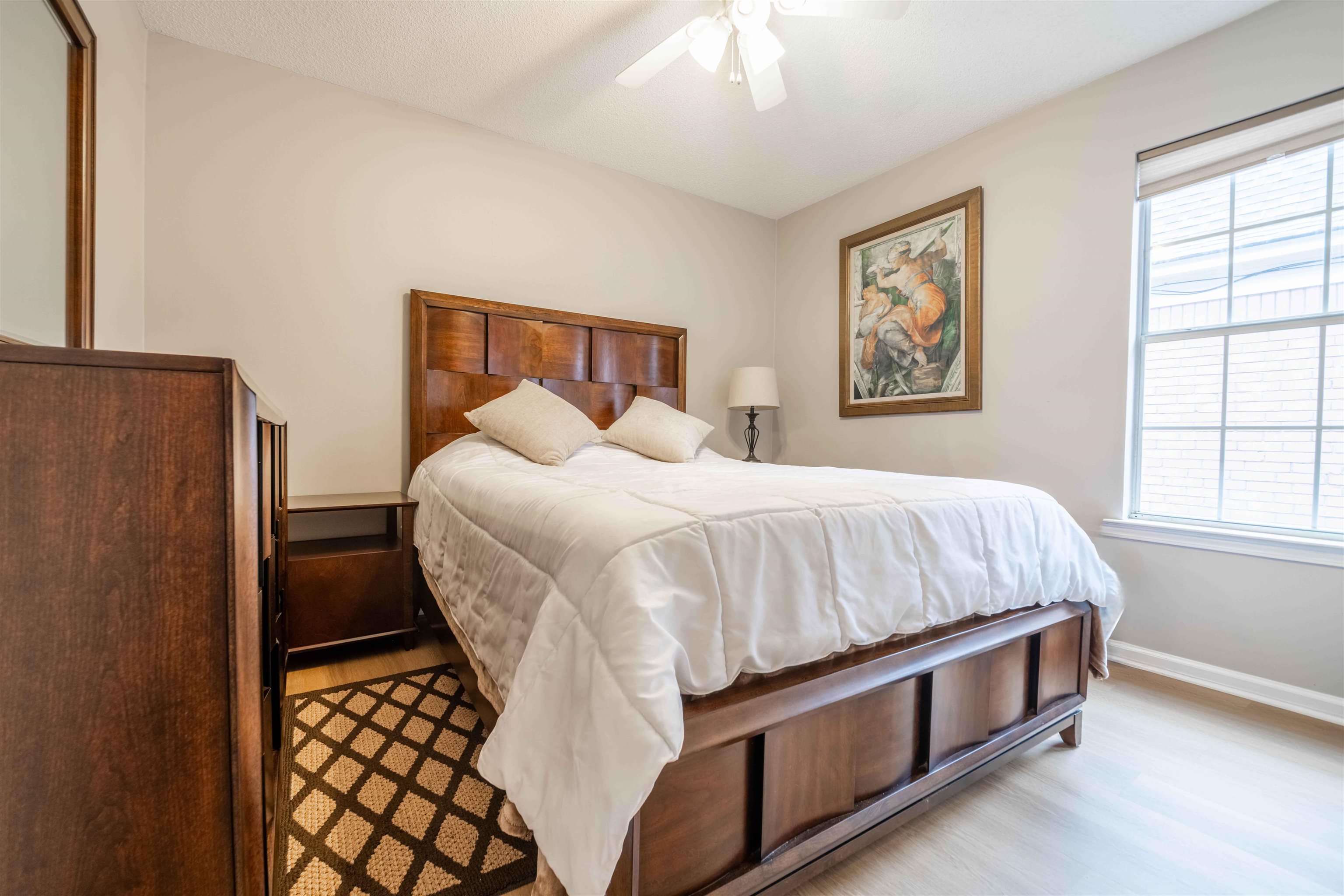 Bedroom with a dark wood bed, white bedding, patterned rug, and bright window.