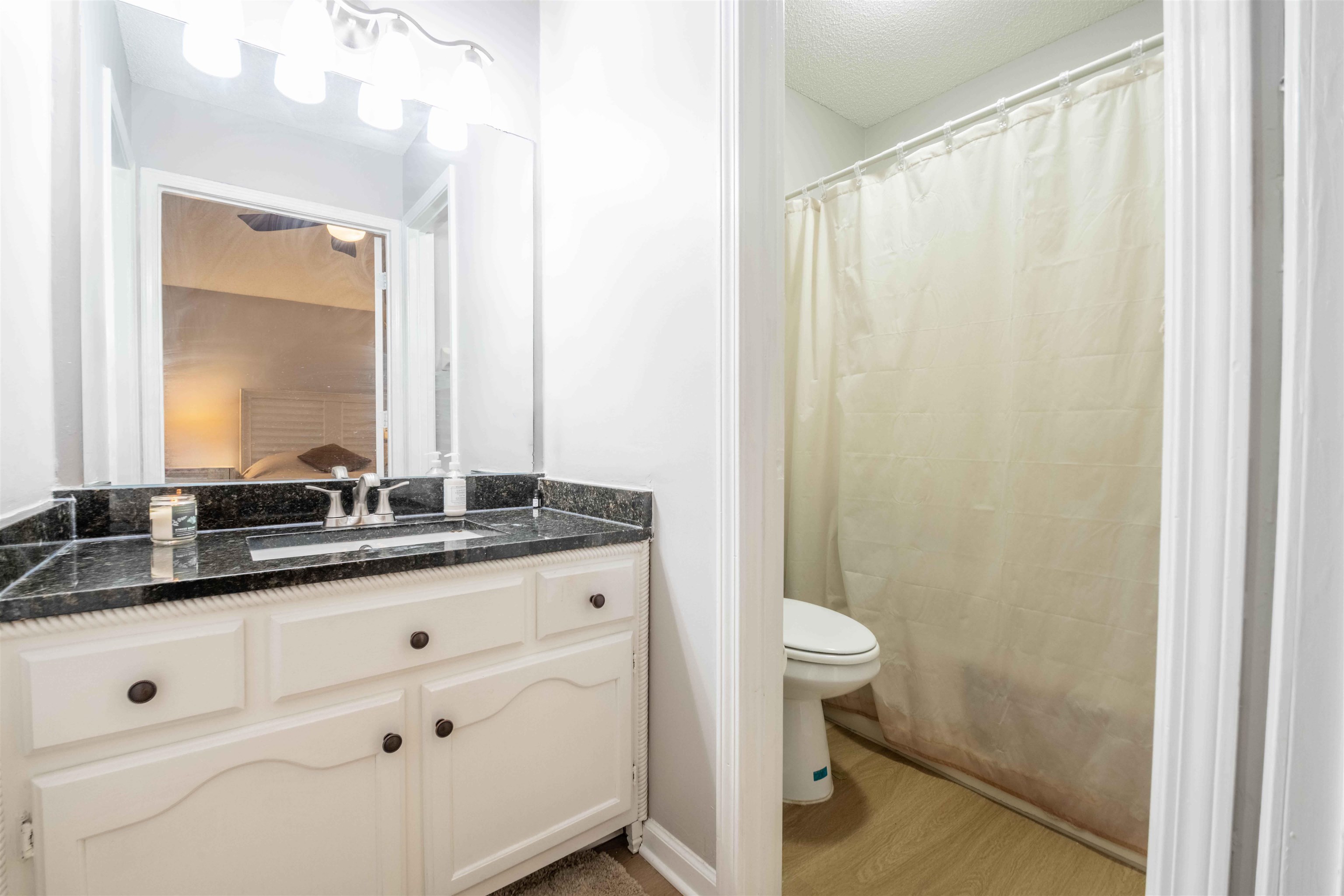Bathroom with a white vanity and black granite counter beside a curtained shower.
