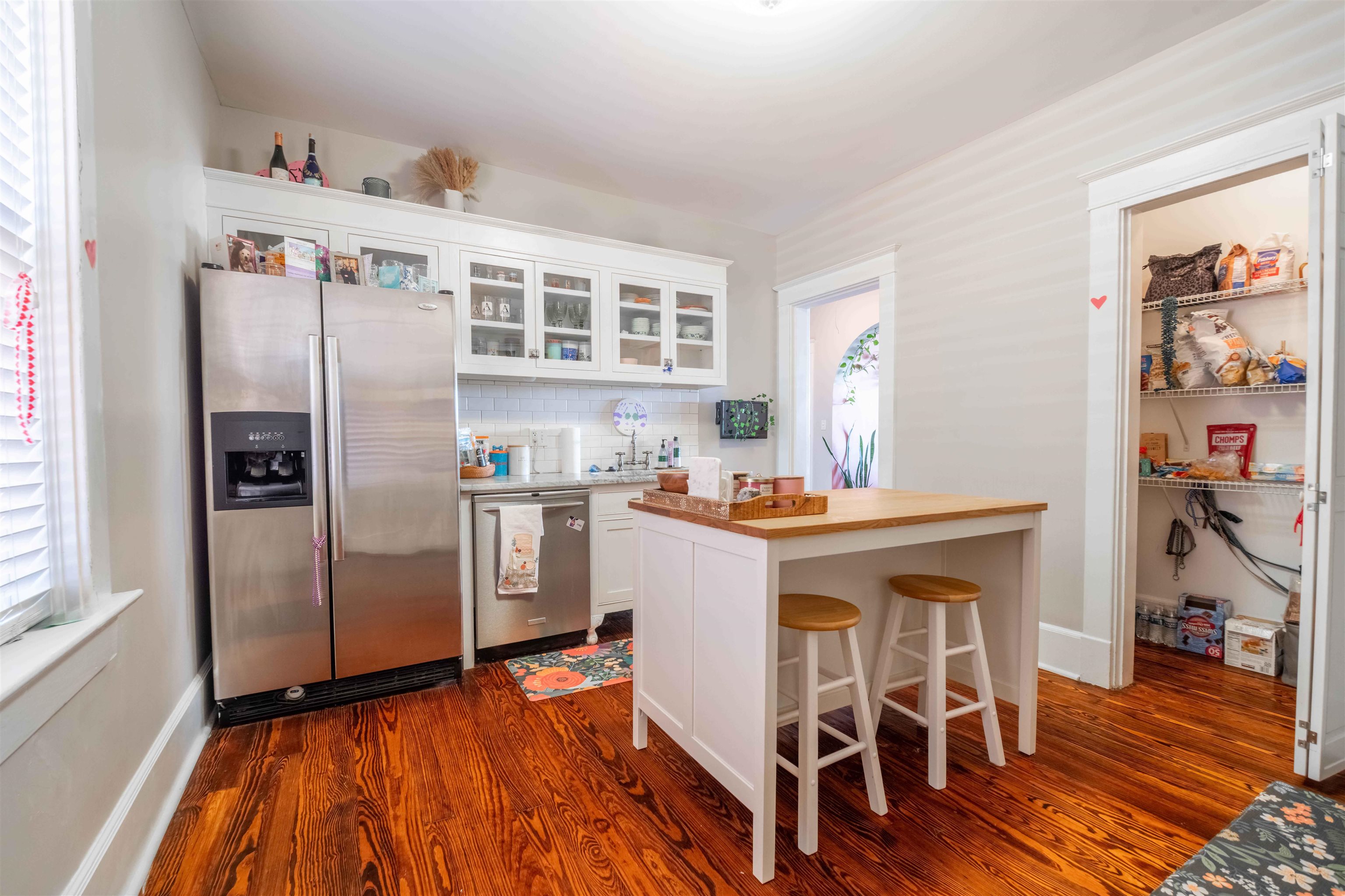 Kitchen with white cabinetry, stainless steel appliances, butcher-block island, and warm hardwood floors.