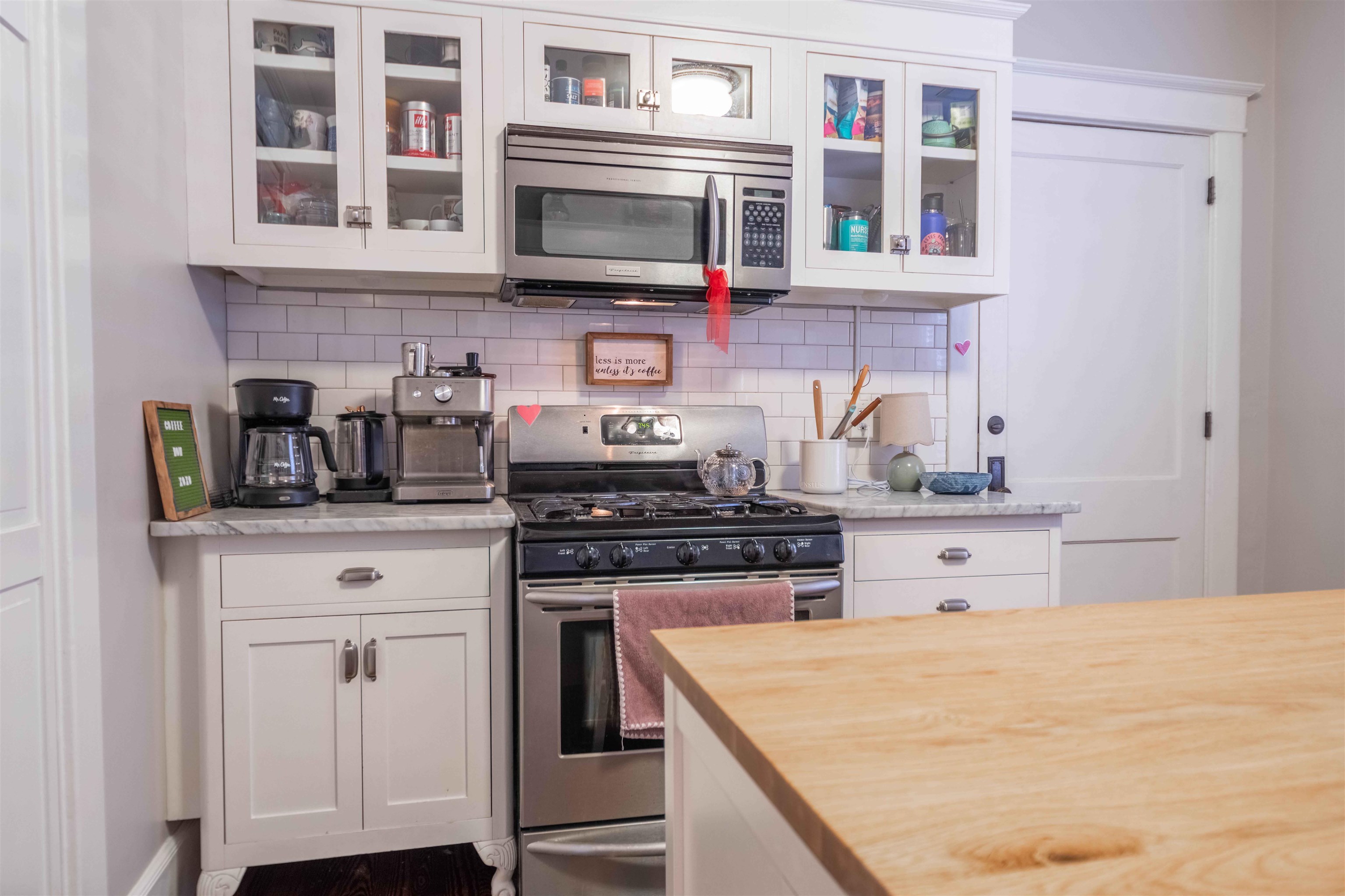 Kitchen with white cabinets, stainless steel appliances, subway-tile backsplash, and a large wood-topped island.