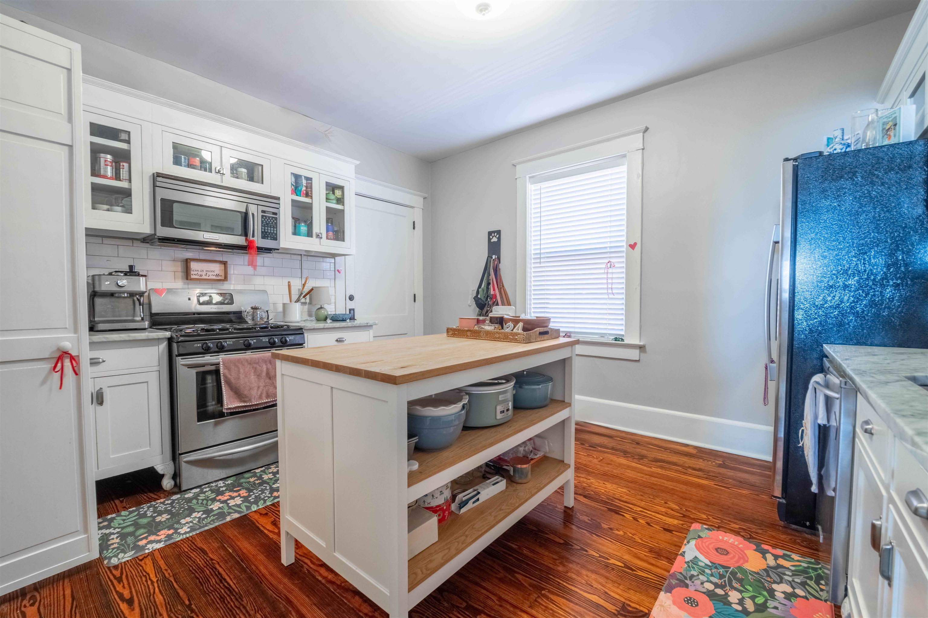 Kitchen with white cabinetry, stainless steel appliances, a butcher-block island, and dark hardwood floors.