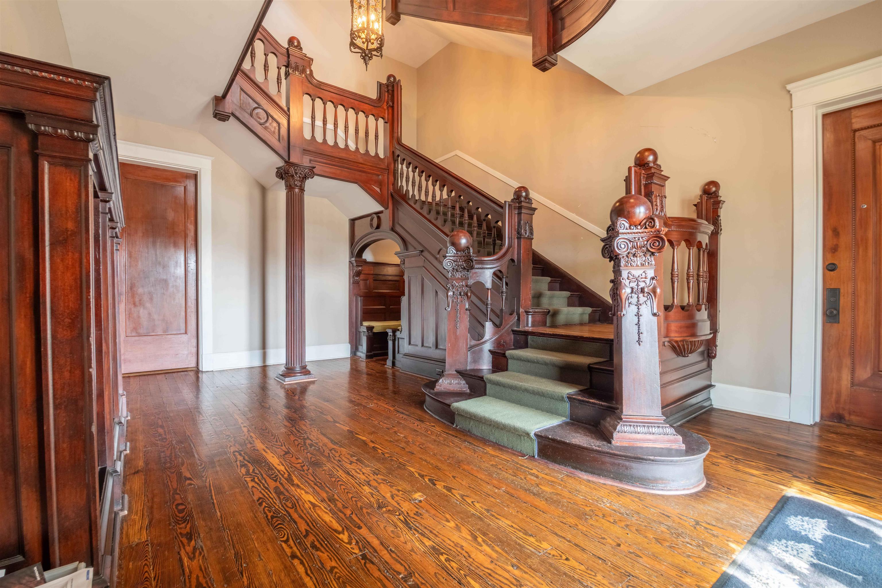 Foyer with an ornate carved wood staircase, green runner, and polished hardwood floors.