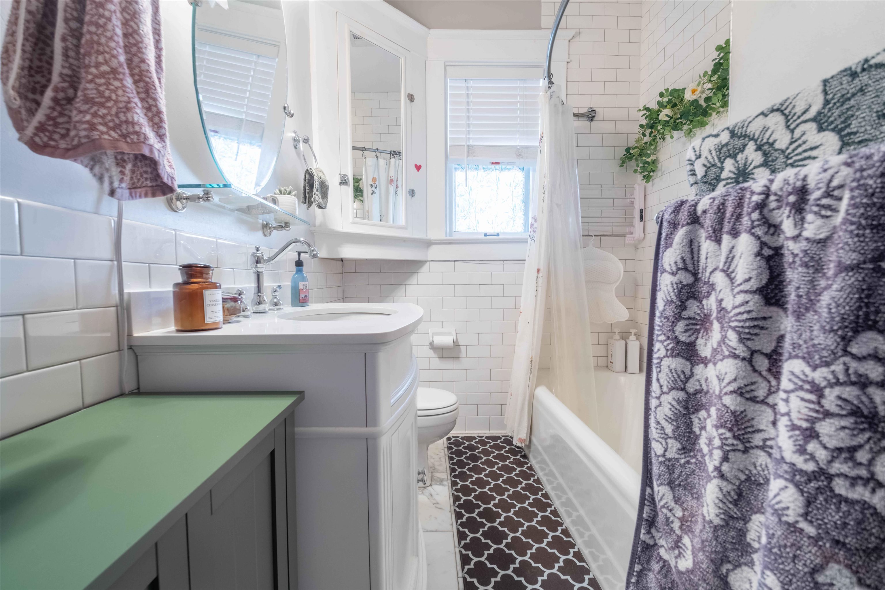 Bright tiled bathroom with a curved vanity, bathtub, and patterned floor runner