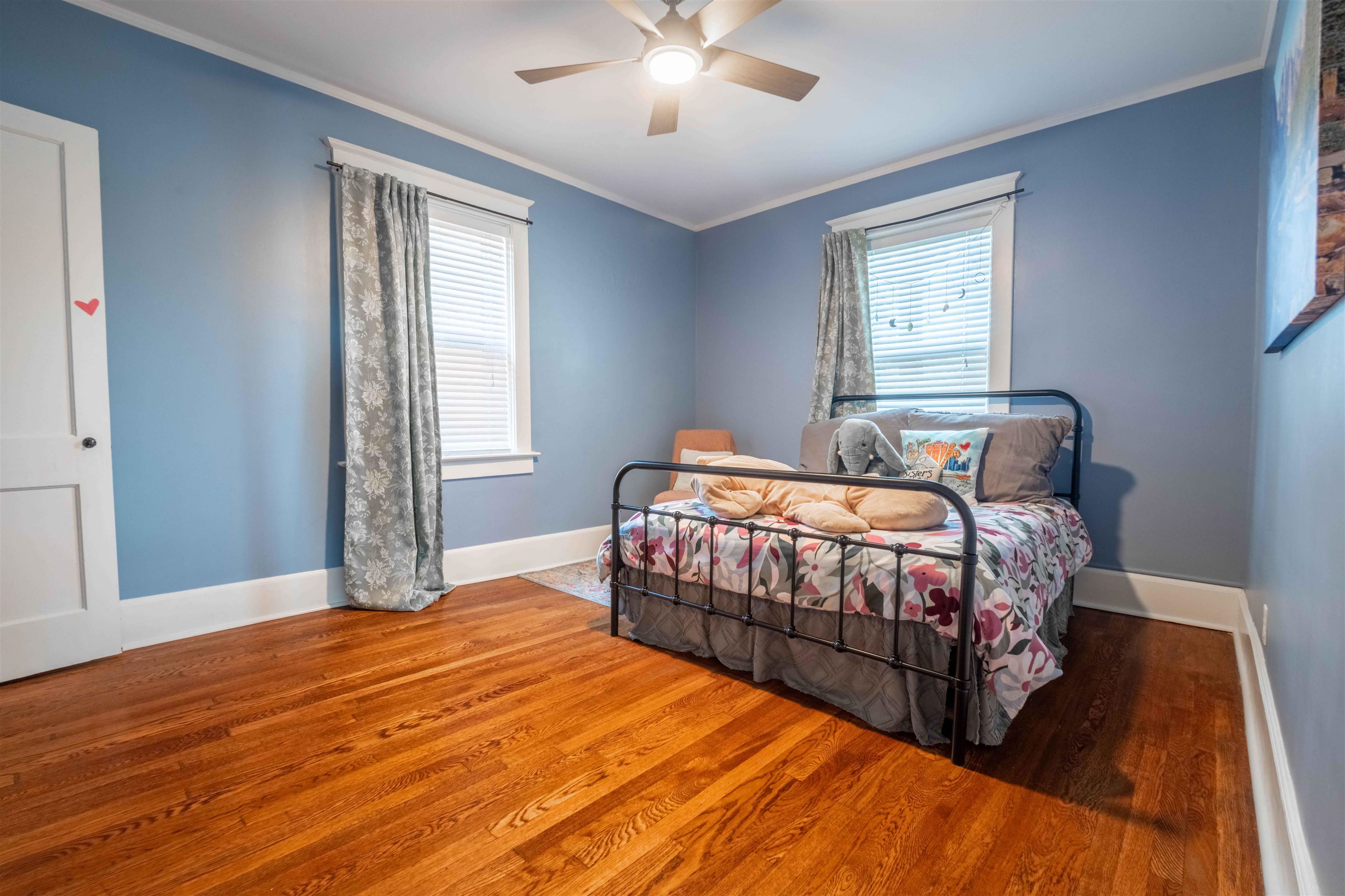Bedroom with blue walls, a metal bed with floral bedding, and hardwood floors.
