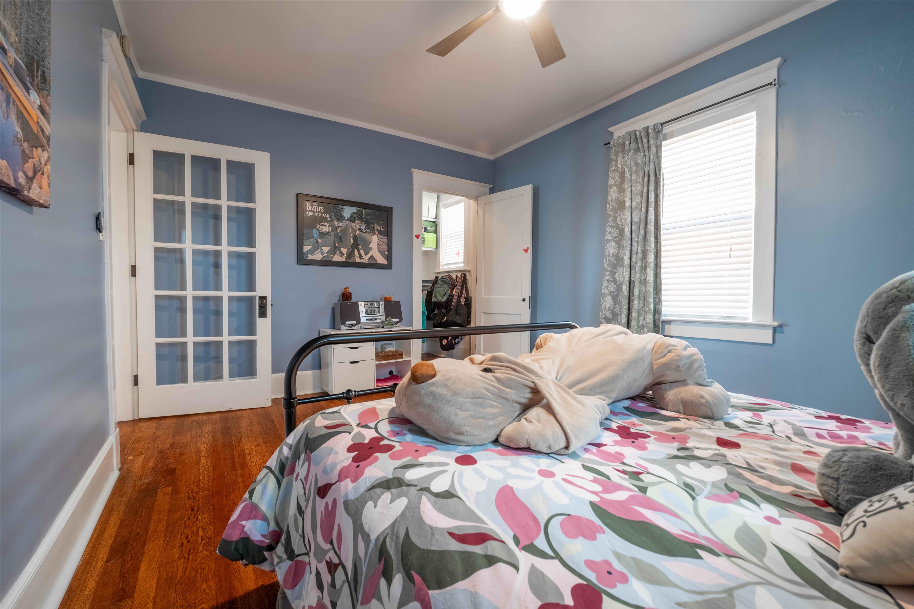 Furnished bedroom with blue walls, hardwood floors, floral bedding, and a large plush dog on the bed.