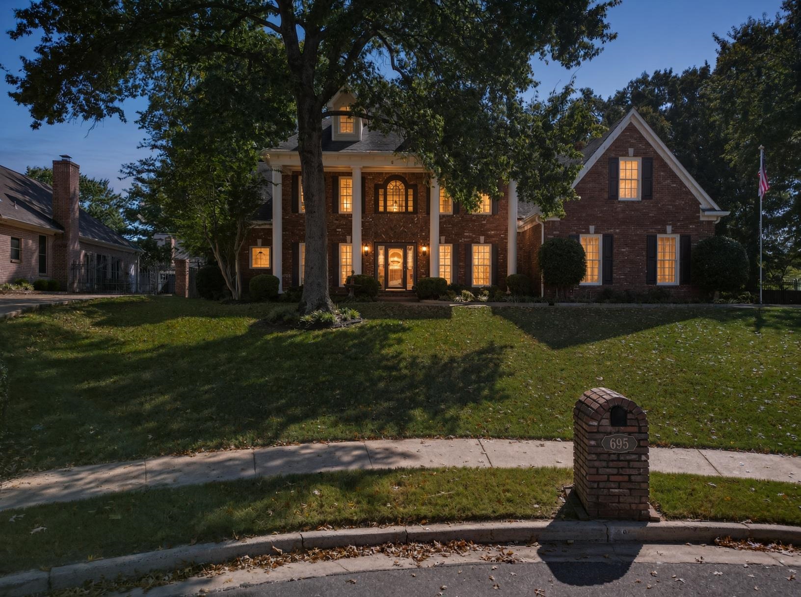 Two-story brick home with white columns, glowing windows, and a front-yard mailbox marked 695.