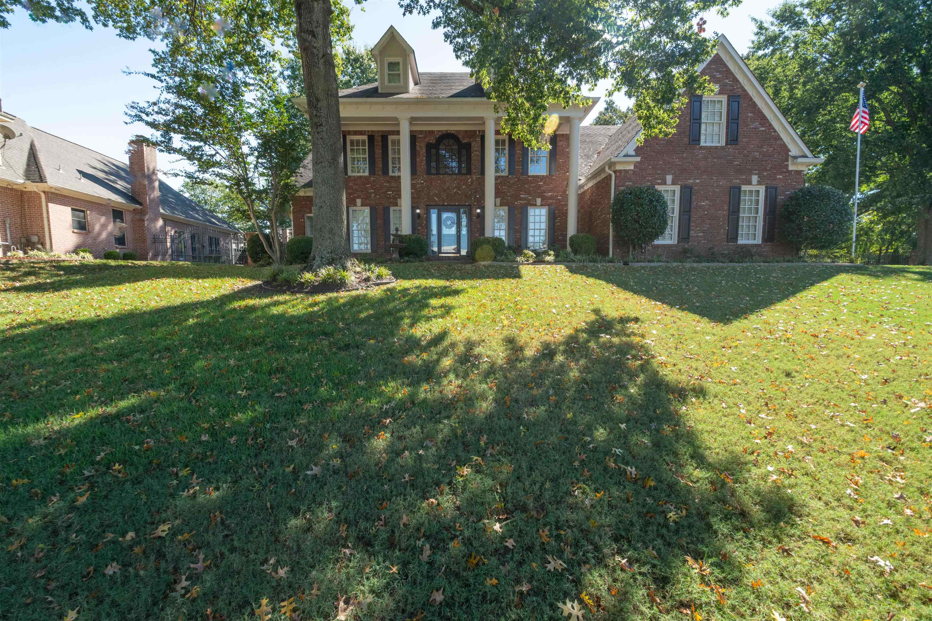 Two-story brick home with a columned front porch and broad leaf-strewn lawn.