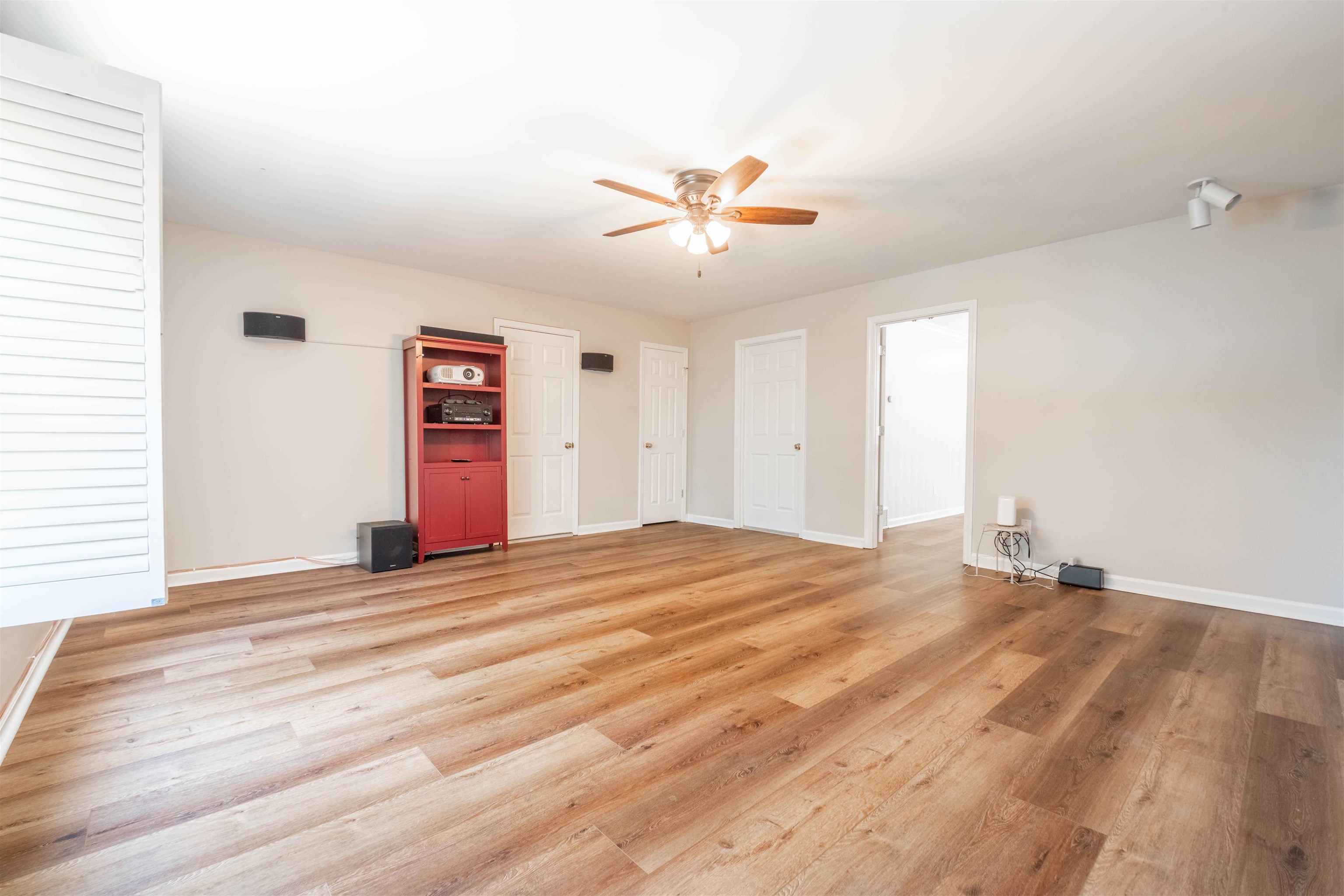 Open room with wood-look floors, a red media cabinet, and ceiling fan.