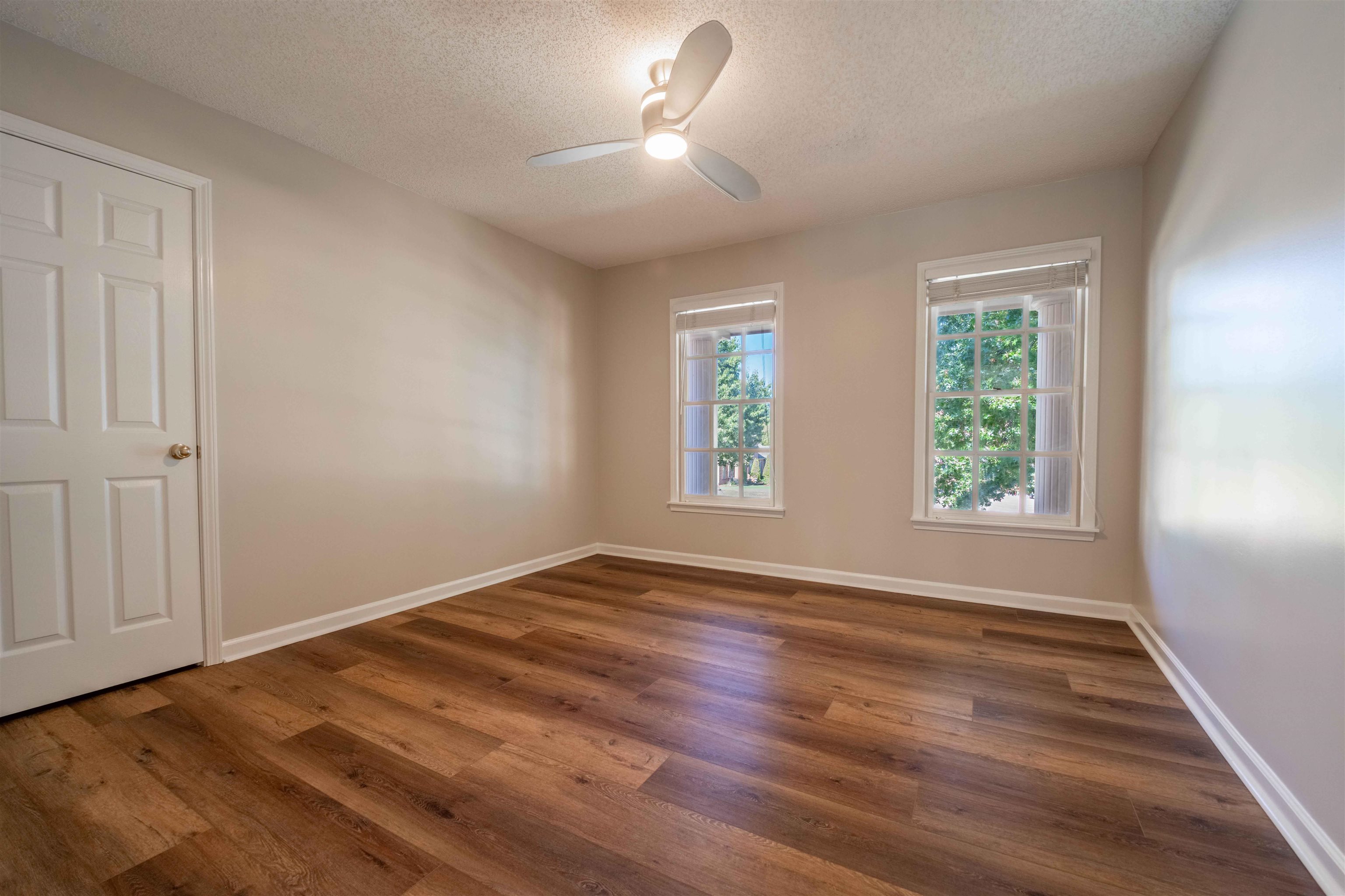 Empty room with wood-look flooring, two windows, and a ceiling fan.